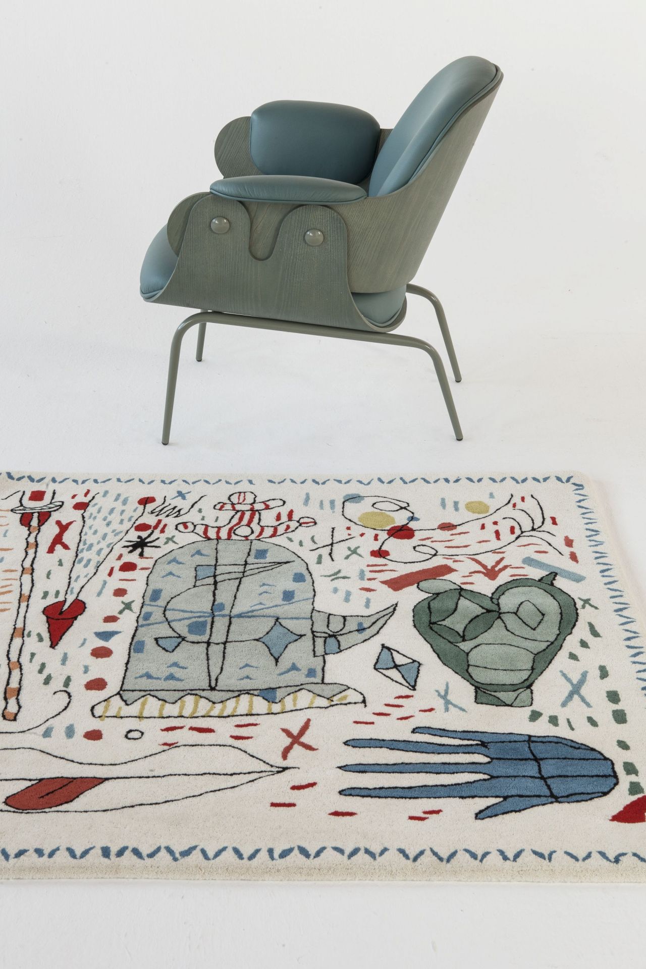 Handgeknüpfter Teppich mit abstraktem Muster in Weiß und bunten Akzenten, kombiniert mit modernem Sessel.