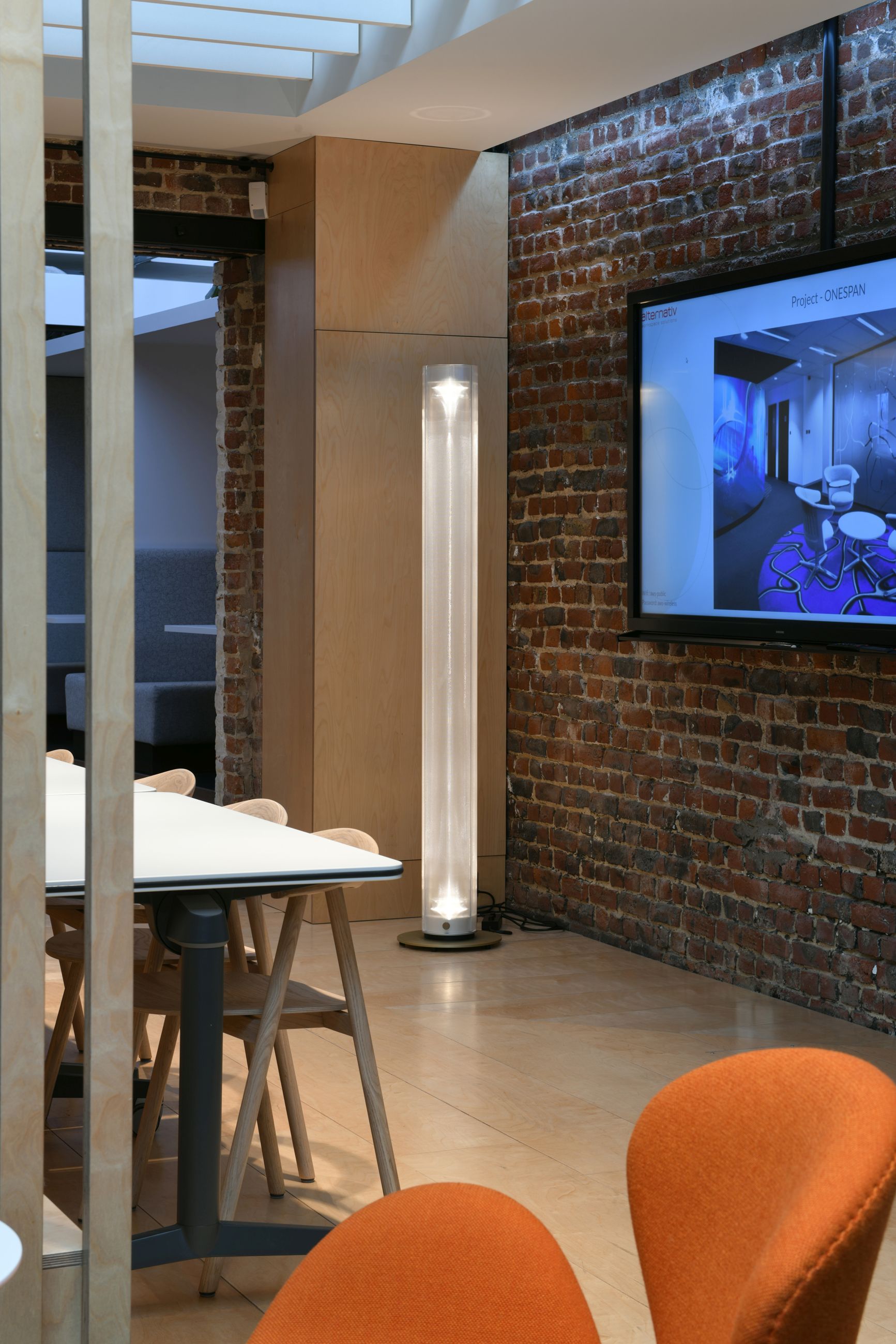 Twilight 360 Stehleuchte von Belux im modernen Büroambiente mit Backsteinwand und Besprechungstisch.
