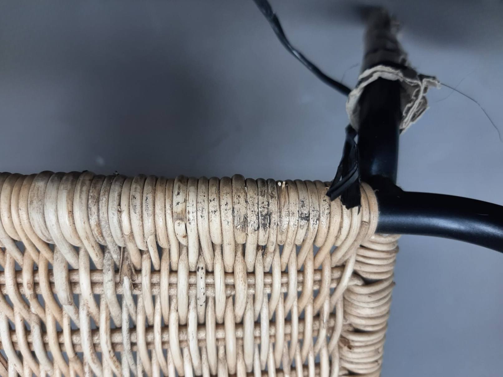 Detailaufnahme des beschädigten Richard Lampert Stuhls TT 54 mit Rattan-Geflecht und schwarzem Metallgestell.