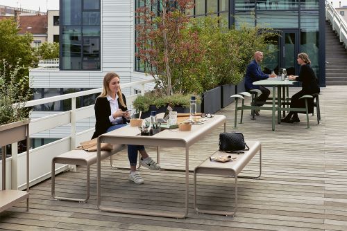 Bolder 2-Sitzer Tisch mit Sitzflächen von Fermob im Außenbereich auf einer Dachterrasse.