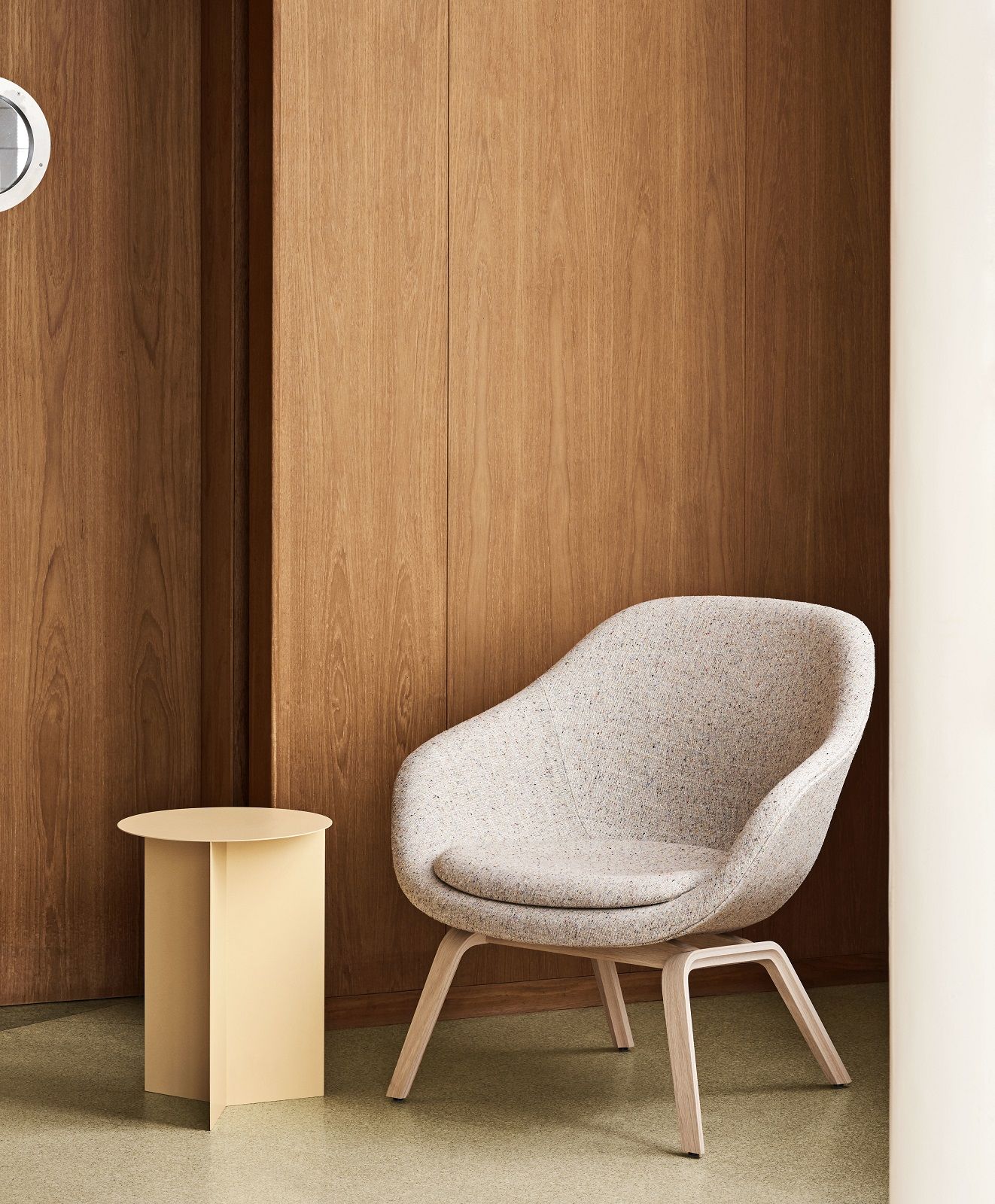 Beiger Hay Slit Table Beistelltisch neben einem Sessel vor einer Holzwand. Moderner Couchtisch.