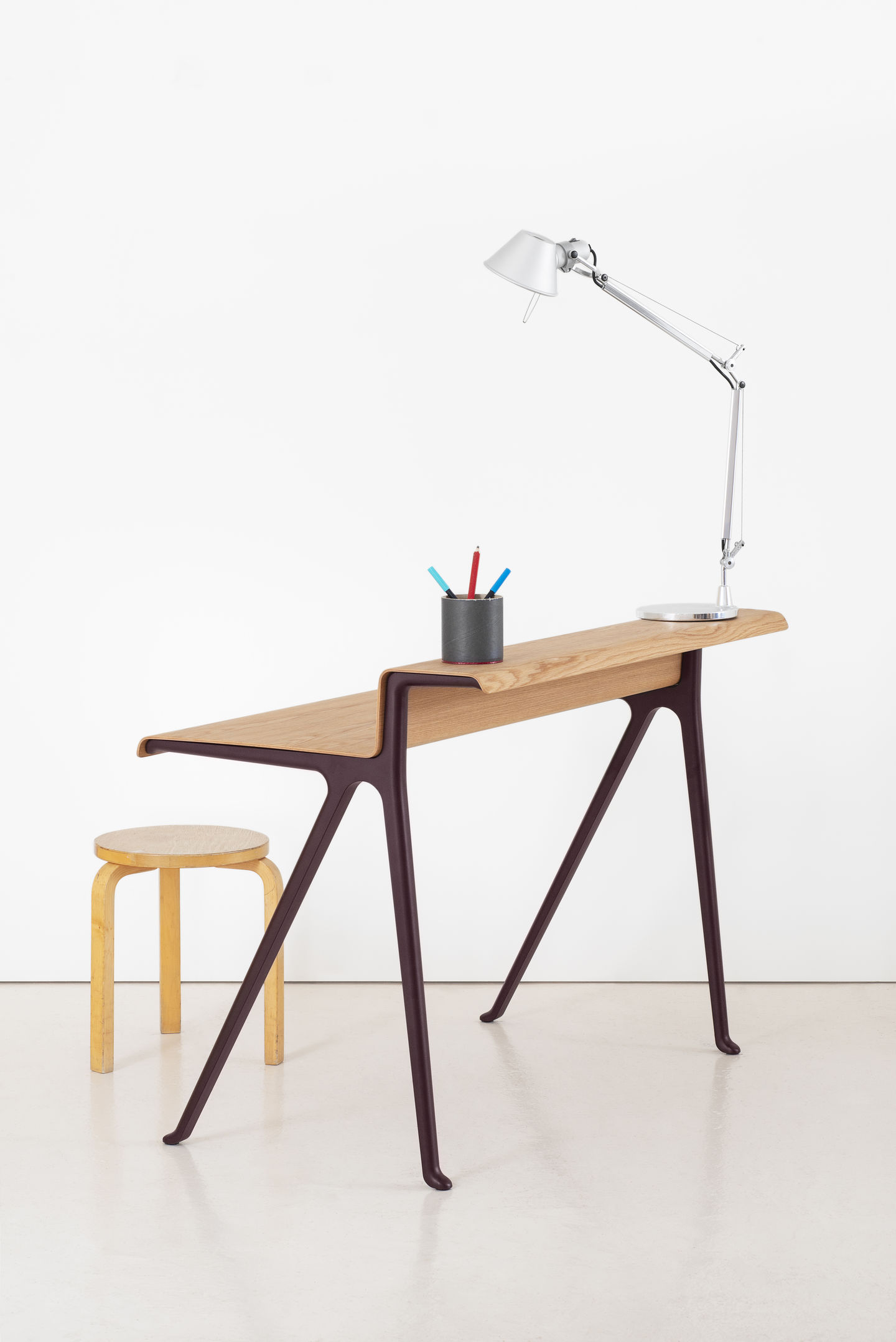 Vitra Courier Schreibtisch aus Holz mit Lampe und Hocker vor weißem Hintergrund.