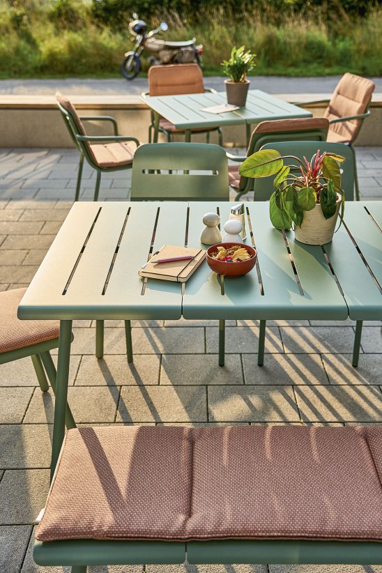 Weishäupl Vapio Tisch Outdoor mit grüner Oberfläche, Stühlen und Bank auf einer Terrasse.