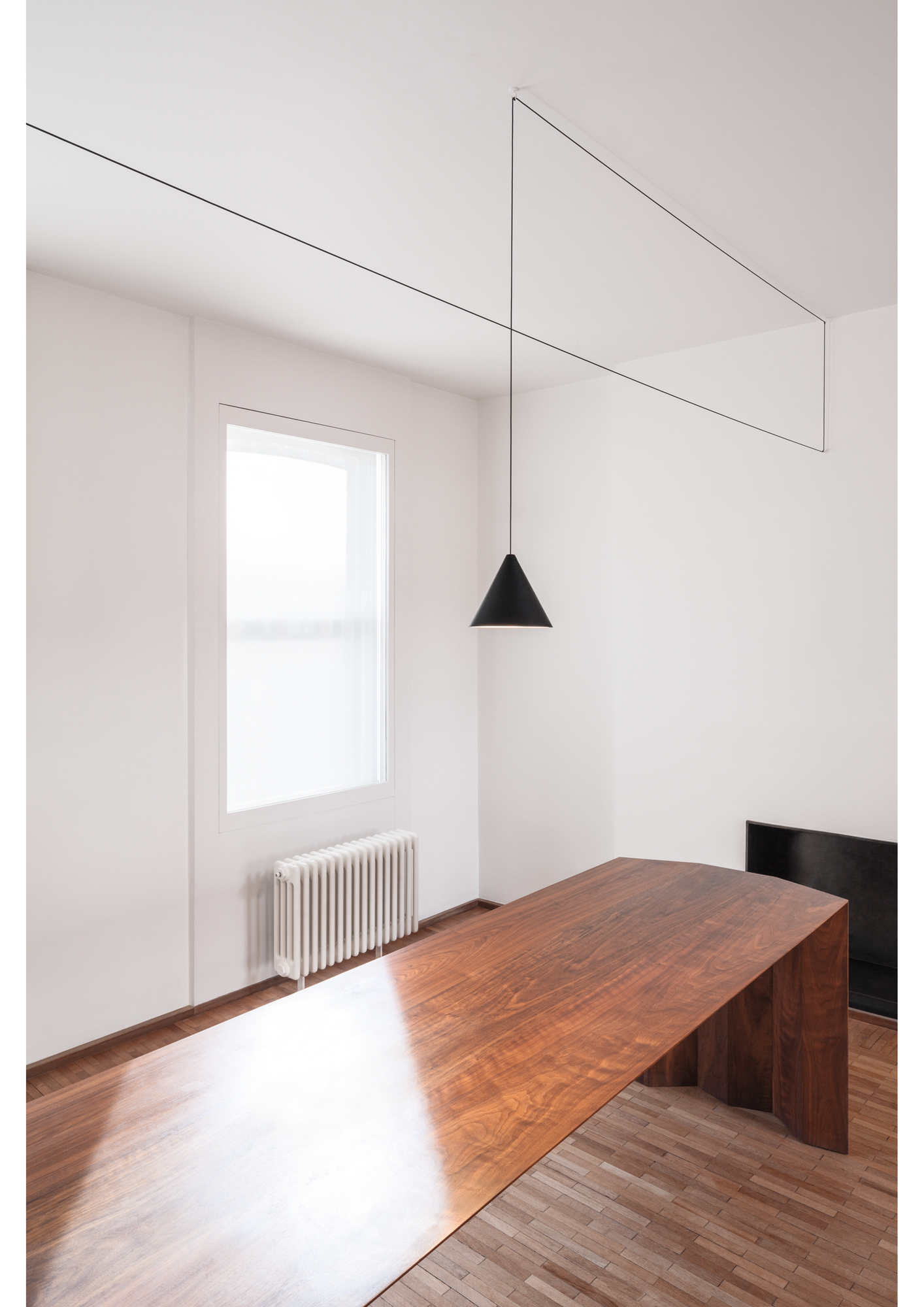 Innenaufnahme mit Flos String Light Kegelkopf Pendelleuchte über einem Holztisch.