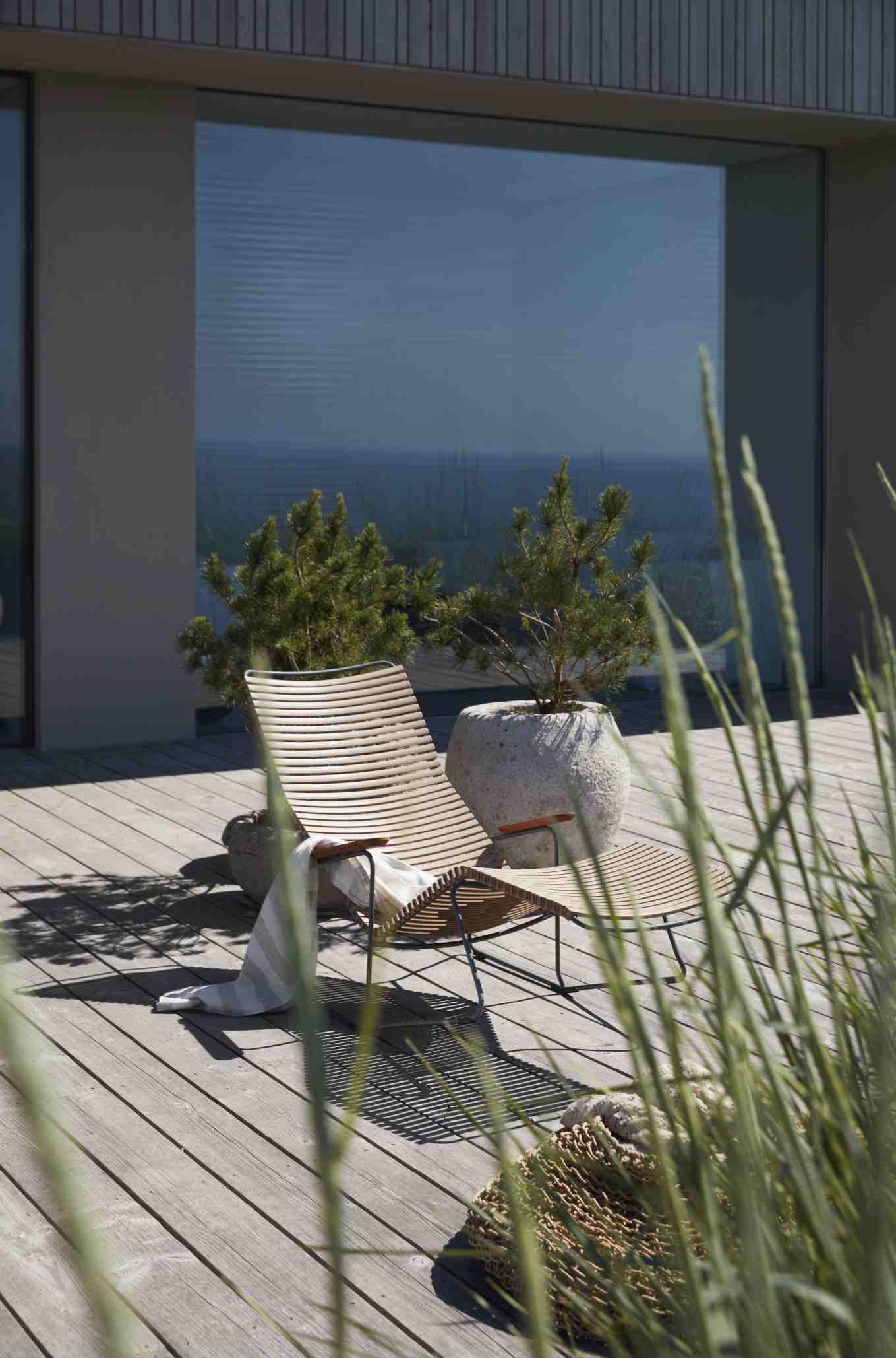 Click Sunrocker Sonnenliege von Houe in Dunkelgrau auf Holzterrasse mit Dekoration und Pflanzen.