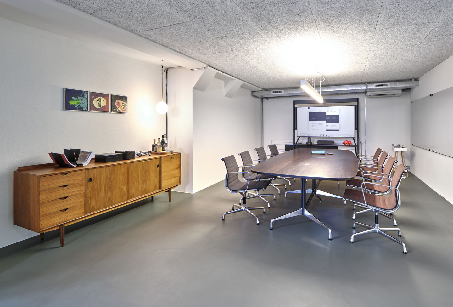 Konferenzraum mit langem Holztisch und Vitra EA 108 Aluminium Stühlen mit braunem und grauem Bezug.