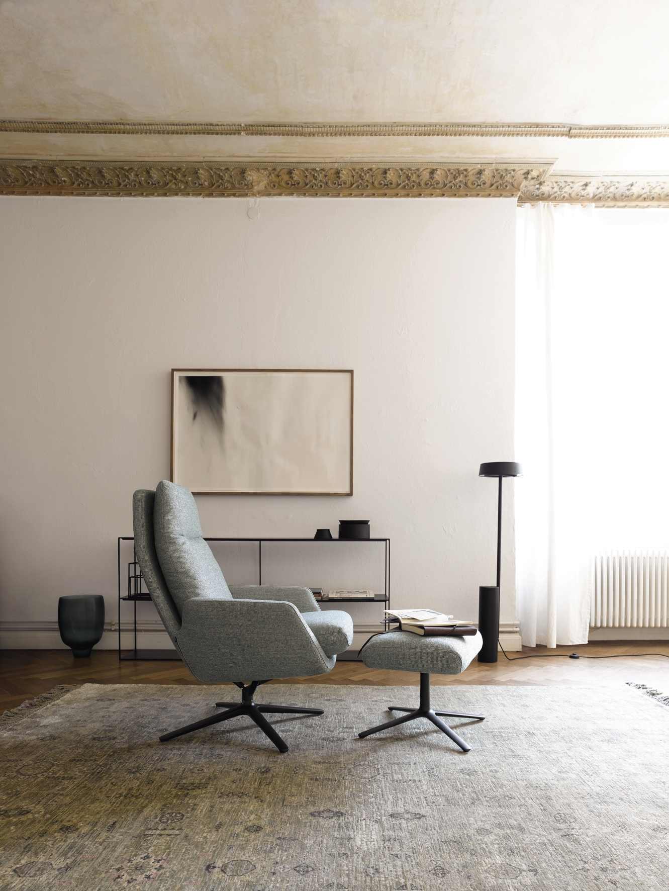 Cordia Drehsessel mit hohem Rücken und passendem Hocker in grauem Stoffbezug im Wohnzimmer.