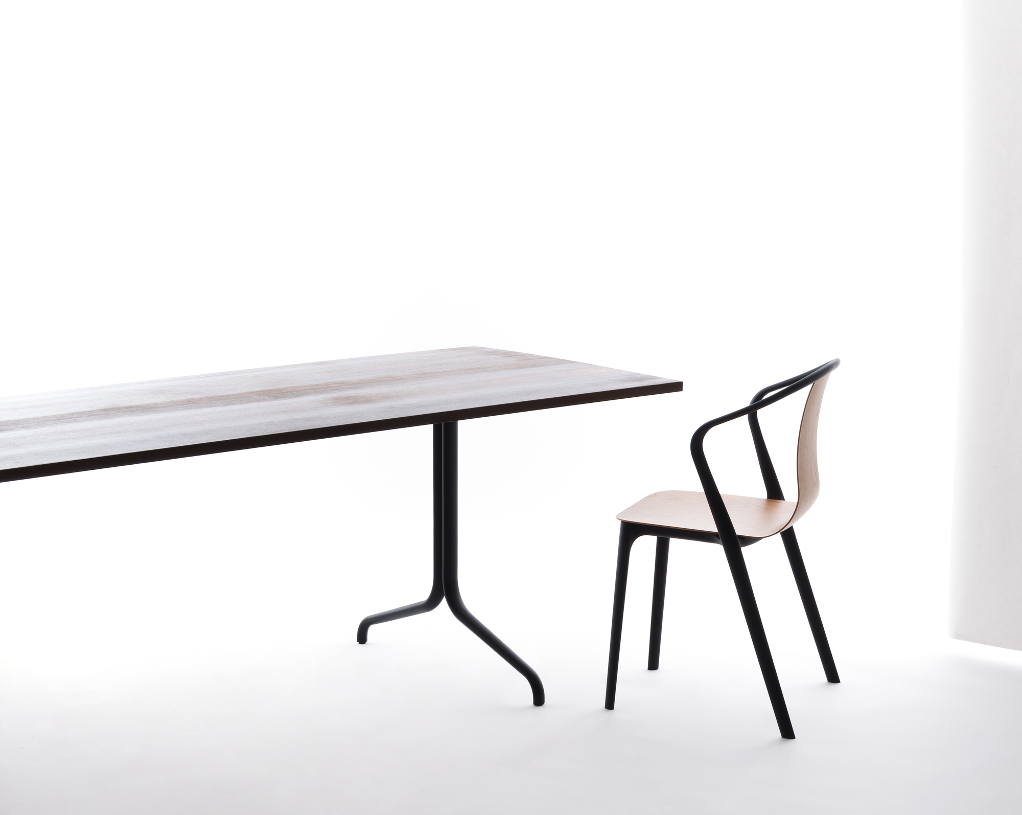 Vitra Belleville Chair Plastic Stuhl neben Esstisch, minimalistisches Design mit schwarzem Gestell und hellem Holz.