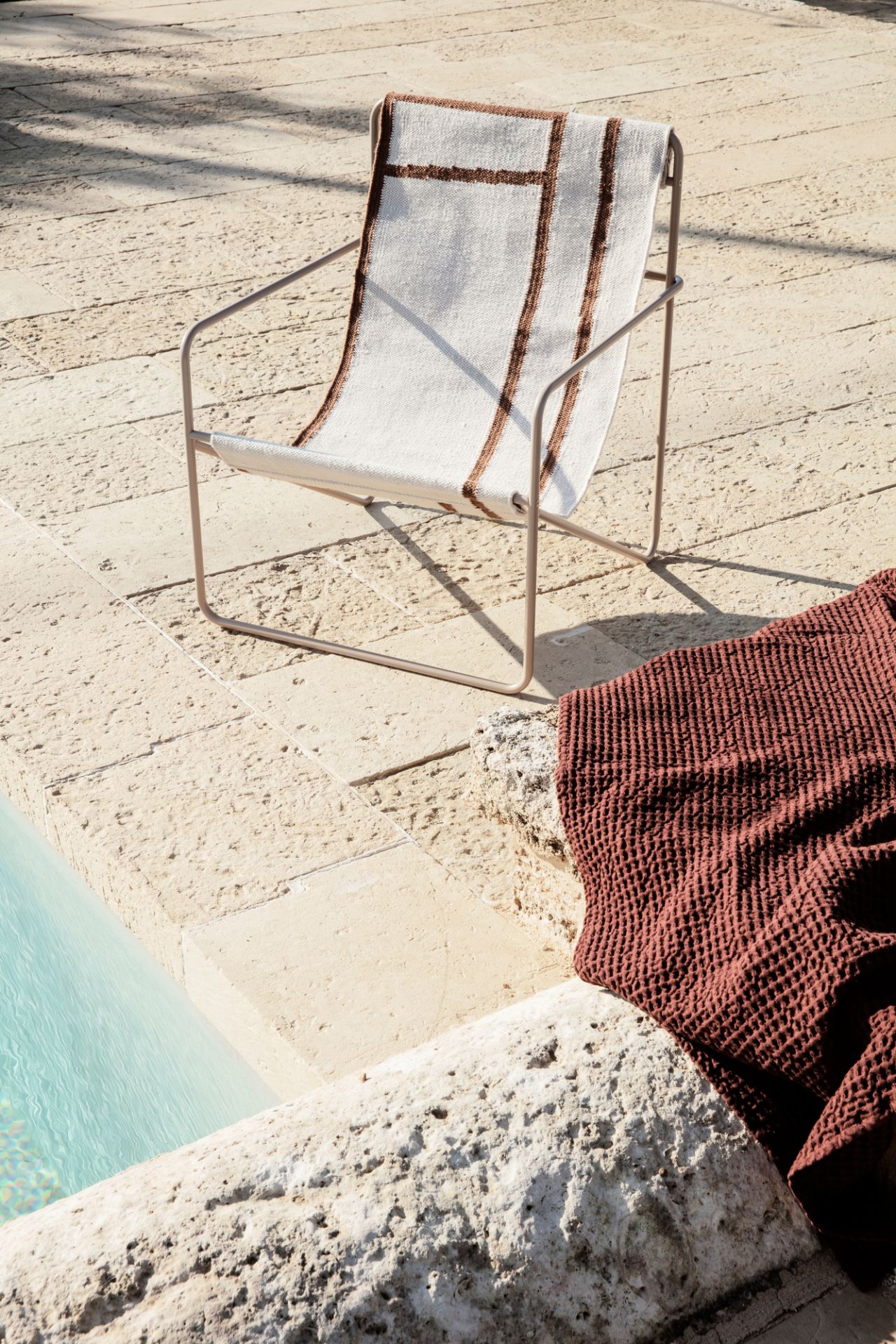 Minimalistischer Outdoor-Sessel mit gestreifter Lehne und braunem Badetuch am Pool. Gartenmöbel für den Sommer.