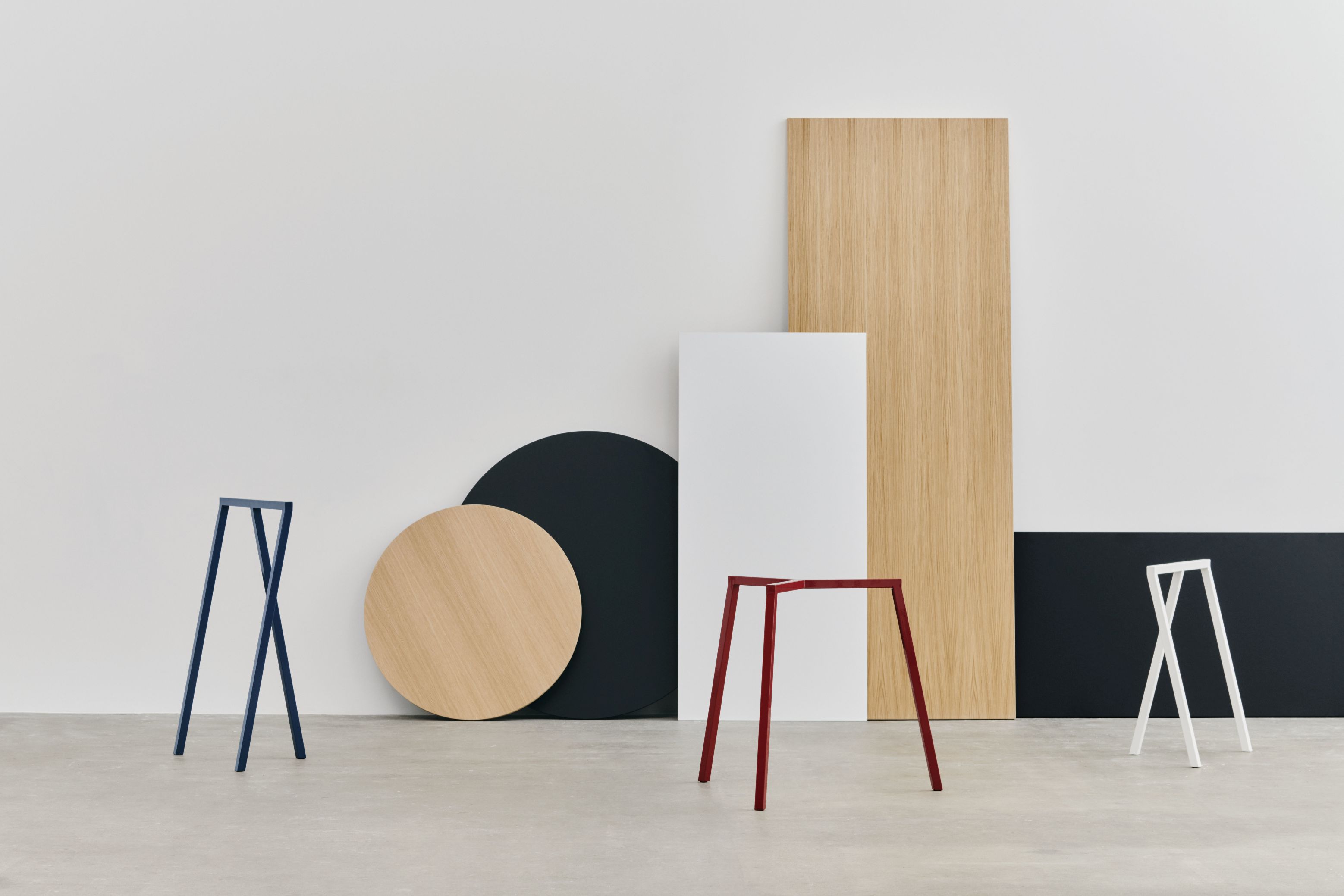 Drei farbige Loop Stand Frame Böcke von Hay vor geometrischen Formen in minimalistischem Design.