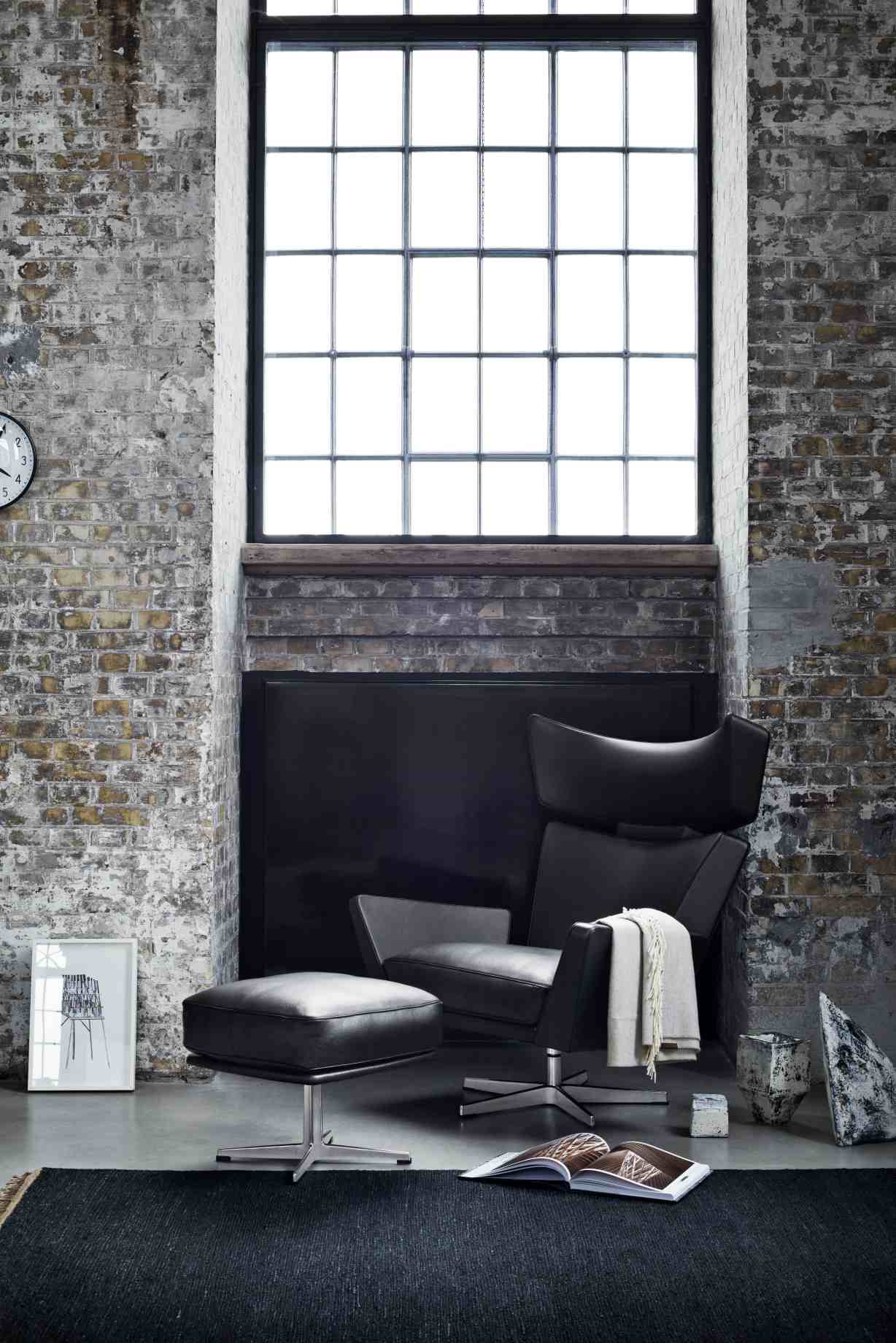 Schwarzer Oksen Sessel von Fritz Hansen mit Hocker in modernem Loft-Ambiente vor Backsteinwand.