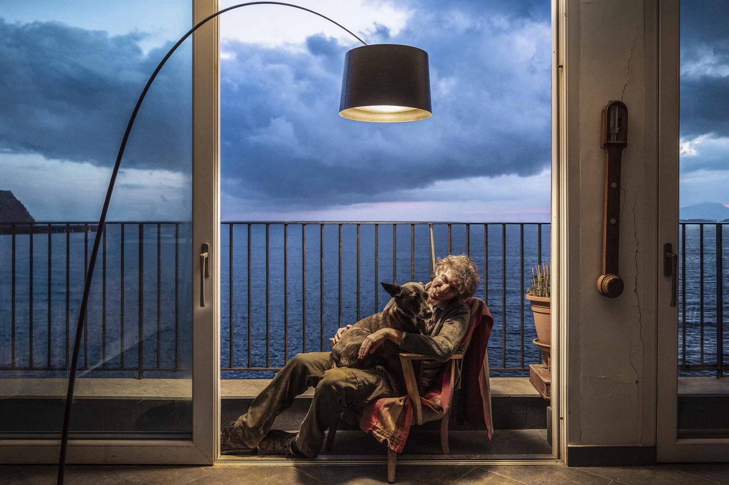 Twiggy Stehleuchte von Foscarini: Frau mit Hund sitzt unter der modernen Bogenlampe mit Schirm am Meer.