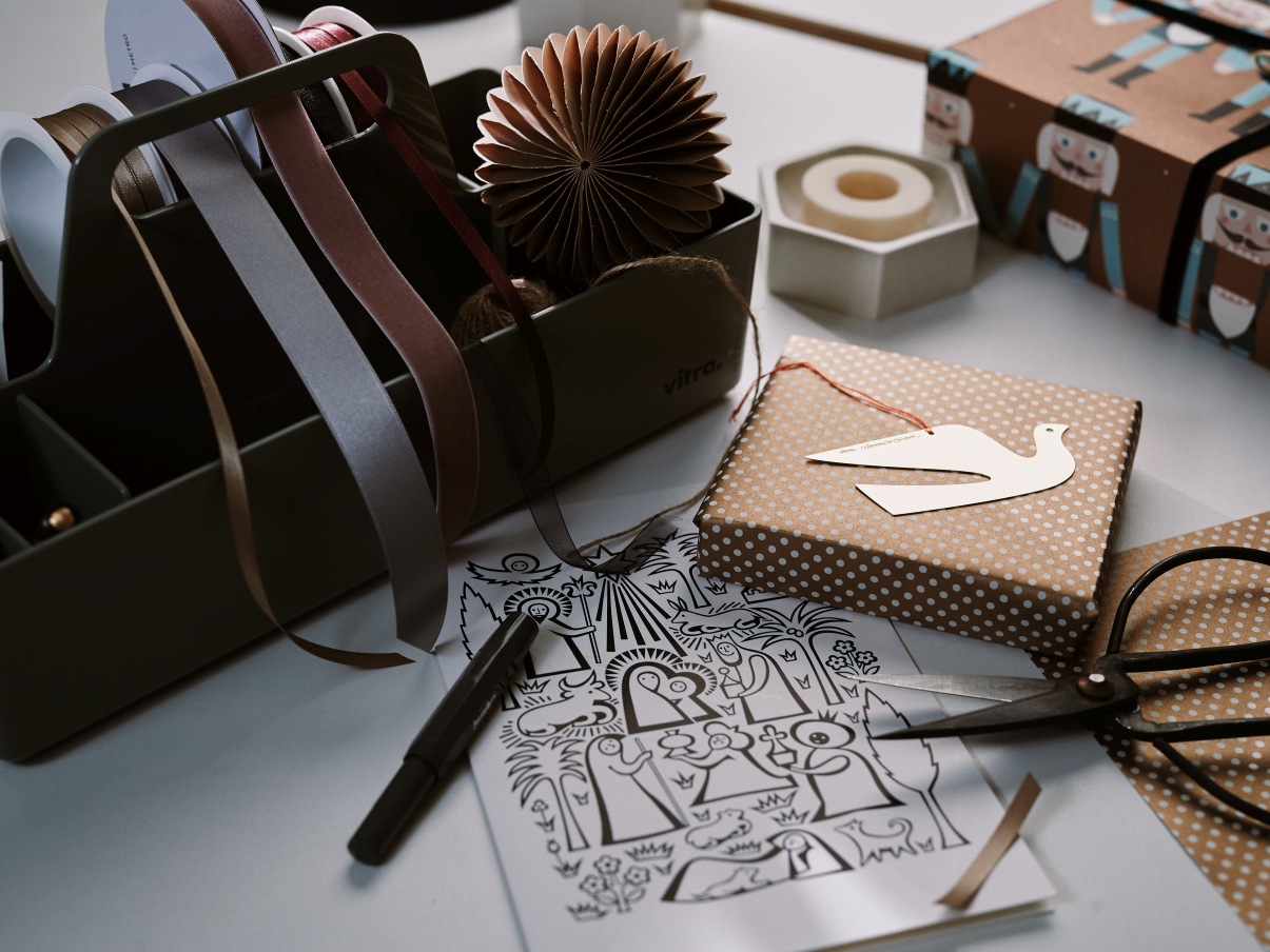 DIY Geschenkverpackung mit Bändern, Schere, Geschenkpapier und Malvorlage für Weihnachten auf einem Tisch.