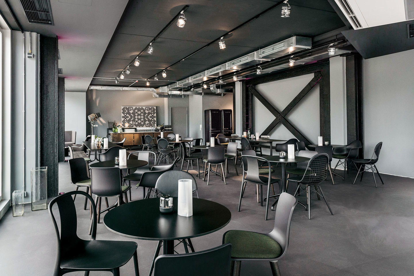 Innenaufnahme eines Restaurants mit vielen Belleville Armchair Wood Stühlen von Vitra an runden Tischen.