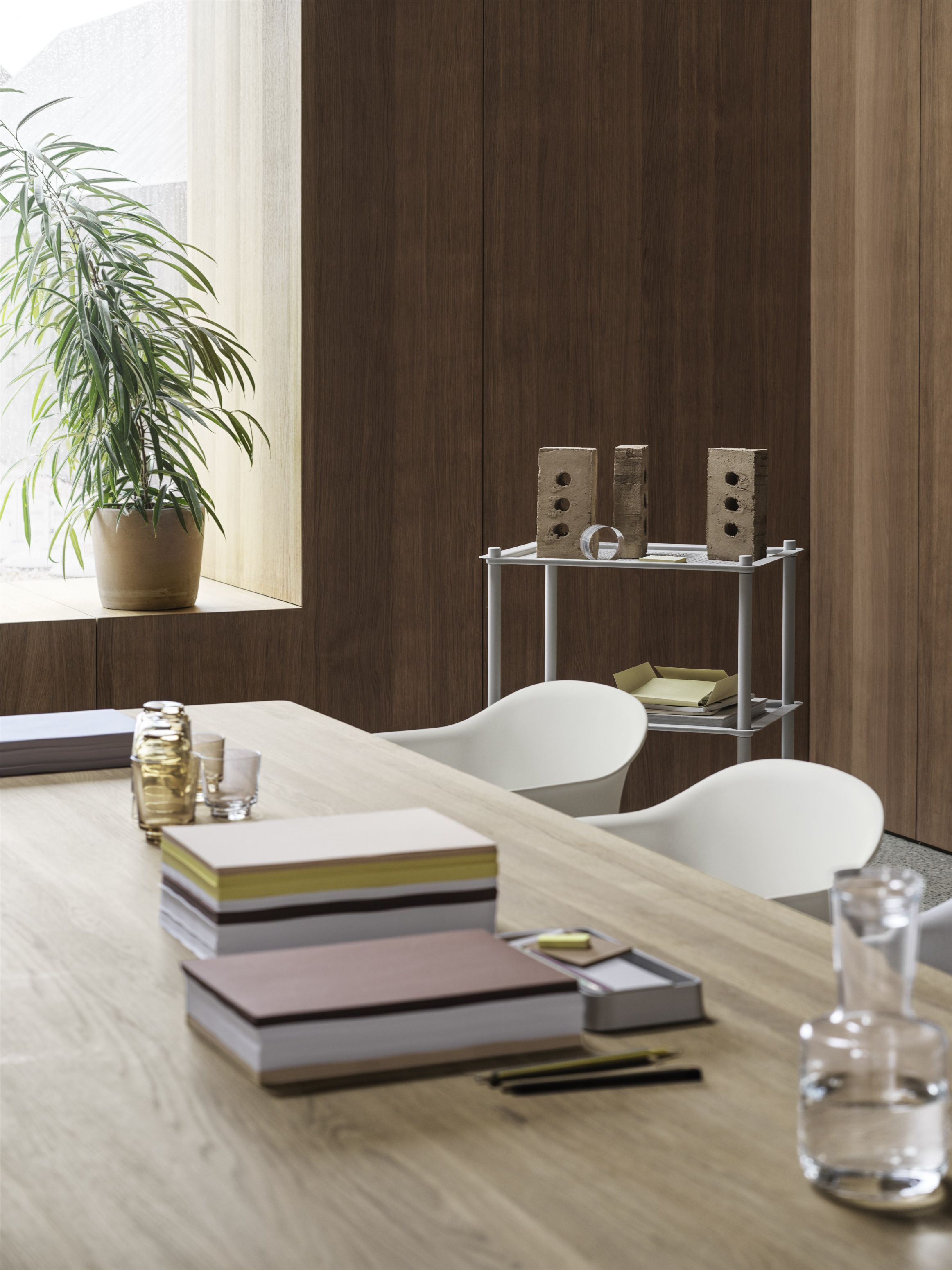 Muuto Fiber Armchair mit Holzgestell in einem modernen Büroambiente, minimalistisches Design, weiße Sitzschale, Holztisch und Regale.