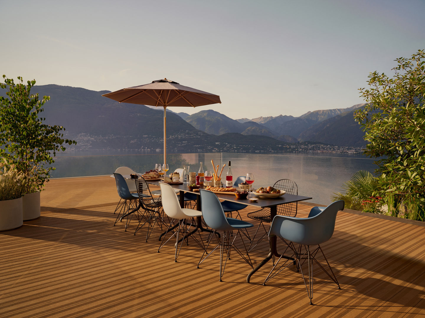 Esstisch im Freien mit ungepolsterten DKR Wire Chairs von Vitra in verschiedenen Farben vor Bergkulisse.