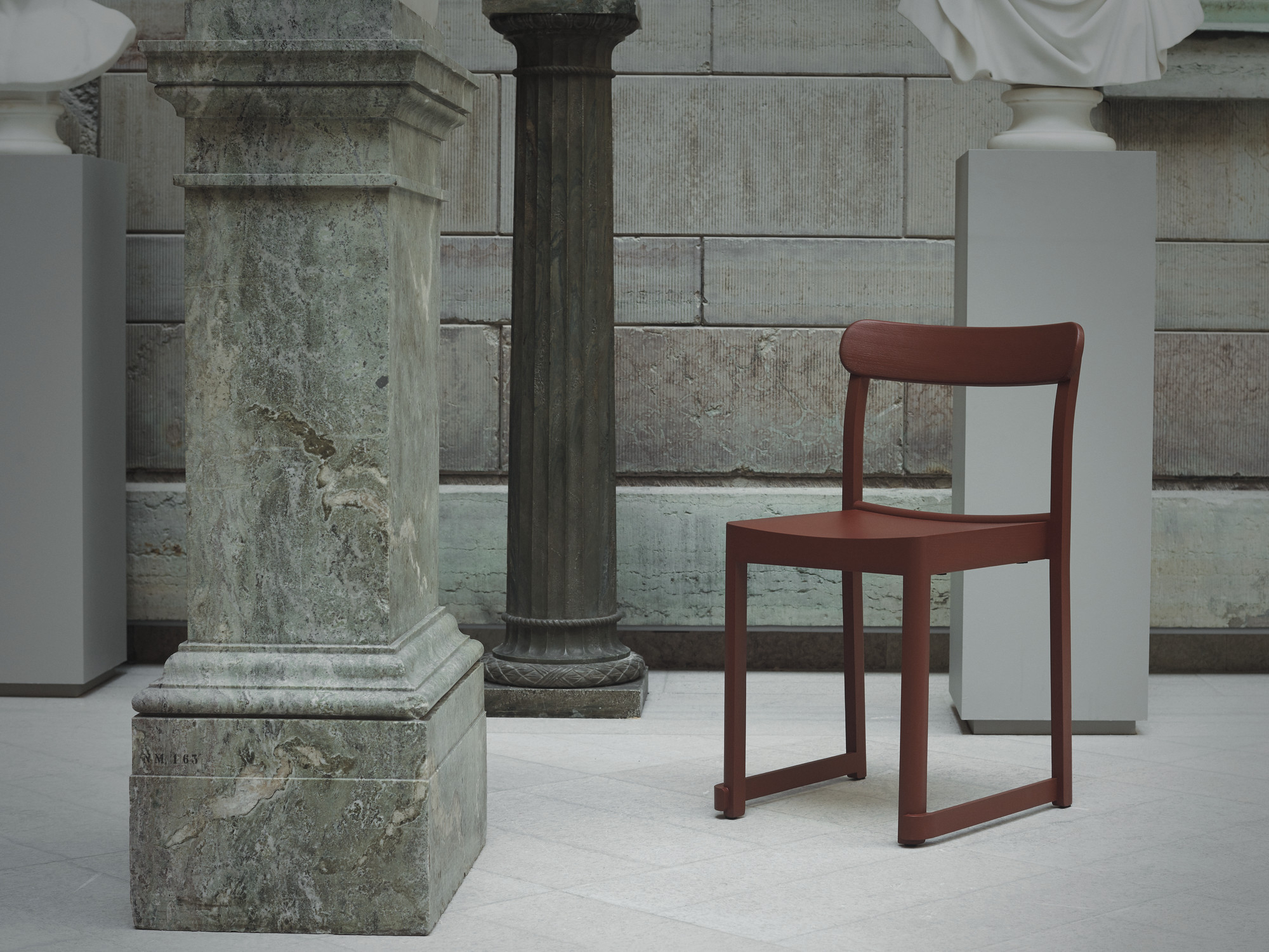 Atelier Chair Stuhl von Artek in Rotbraun vor Säulen und Steinwand.