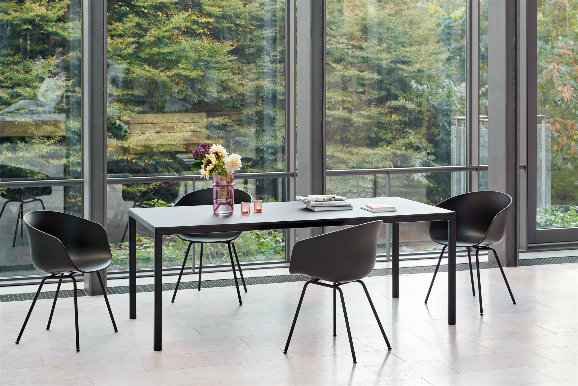 Schwarzer About A Chair AAC26 Stuhl von Hay um einen Esstisch mit Blumen und Büchern.