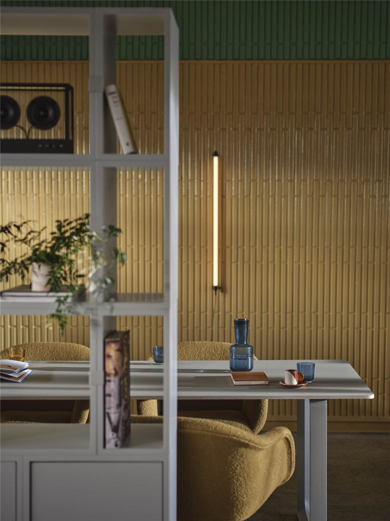 Nahaufnahme der Muuto Fine Wall Wandleuchte, vertikal an gelber Wand montiert, neben modernem Regal.