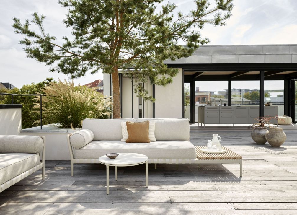 Helle Outdoor-Lounge mit Sofa, Beistelltisch und Holzboden für entspannte Stunden im Freien.