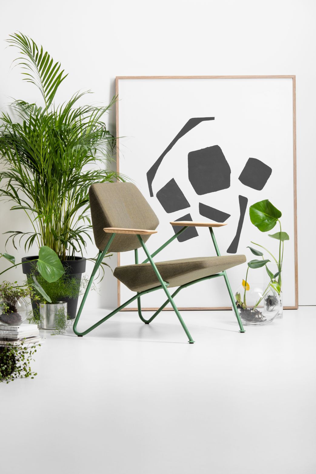 Moderner Sessel mit grünen Metallbeinen, braunem Stoffbezug und Holzarmlehnen, umgeben von Pflanzen. Designermöbel für Wohnzimmer.