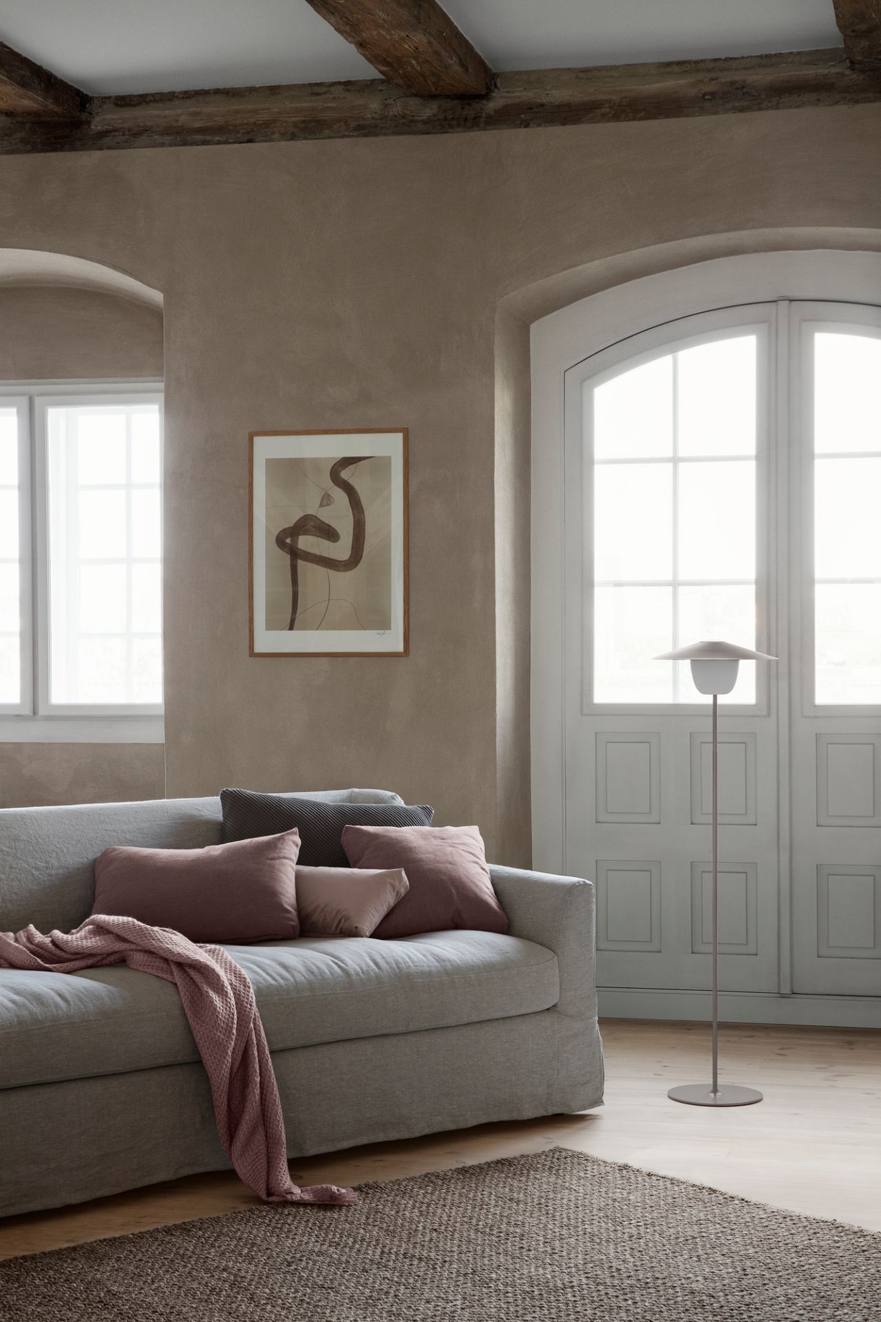 Helle Stehleuchte neben grauem Sofa mit Kissen und Decke in modernem Wohnzimmer mit Teppich.