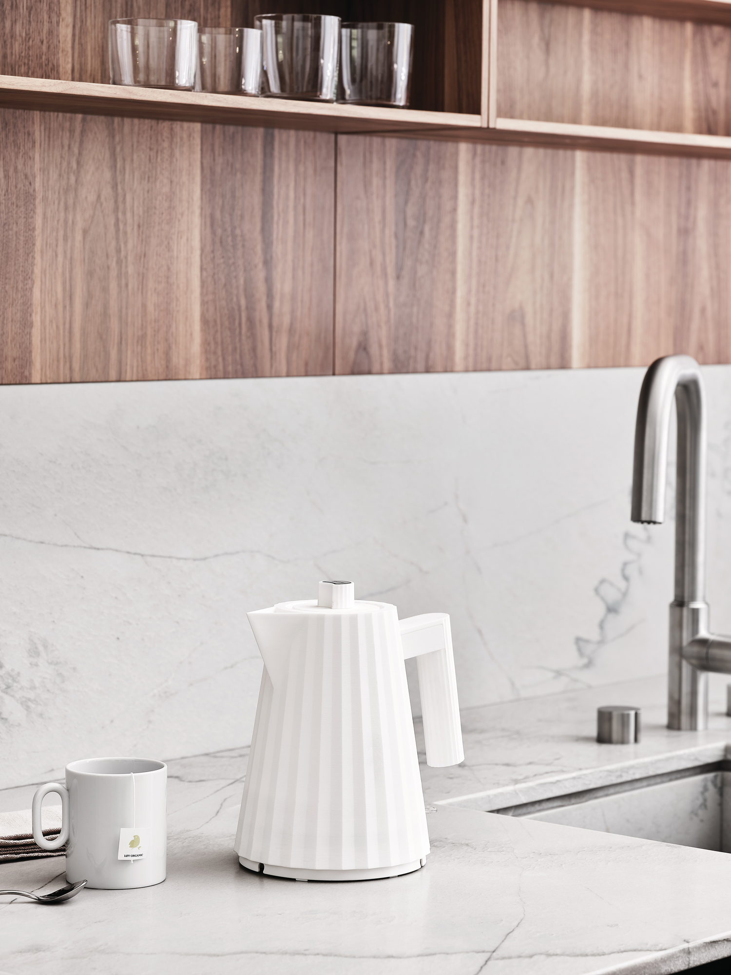 Weißer Alessi Plissé Wasserkocher auf einer Marmor-Küchenarbeitsplatte neben einer Tasse Tee. Design Wasserkocher für die Küche.