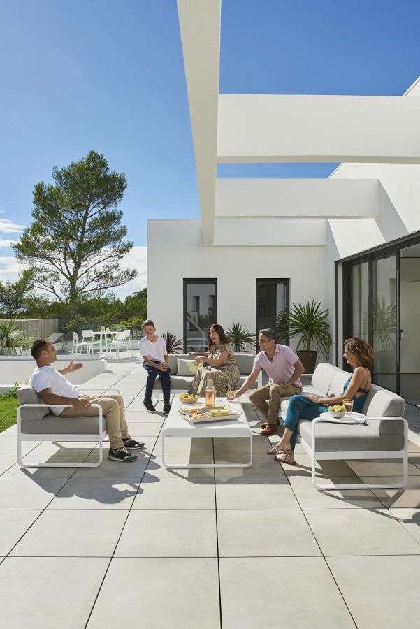 Familie entspannt am Bellevie Outdoor Tisch von Fermob auf einer modernen Terrasse.