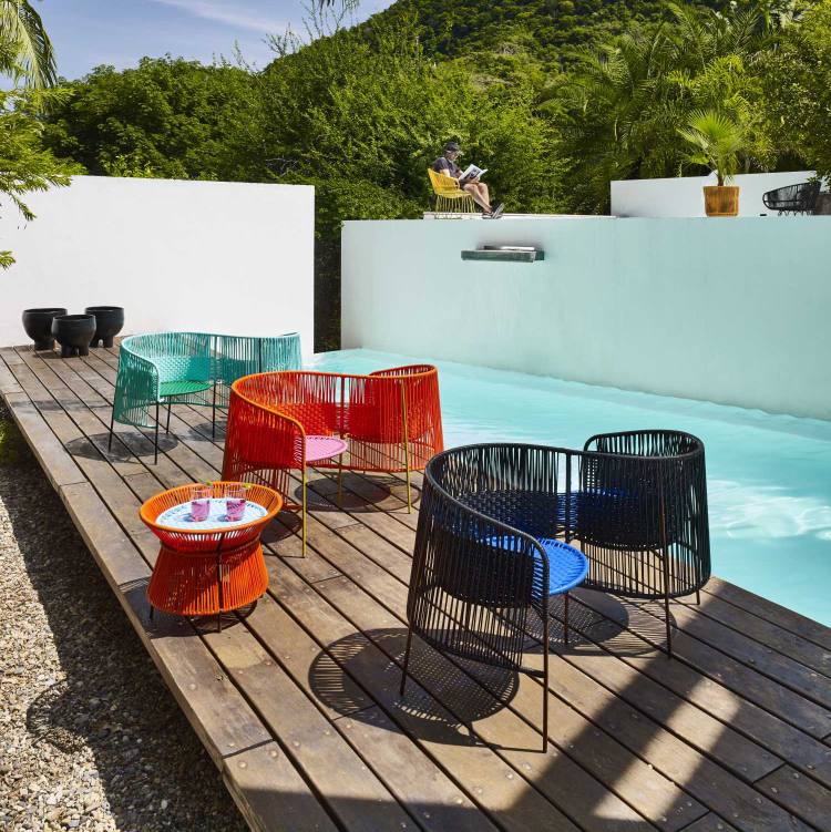Ames Caribe Basket Table und farbenfrohe Outdoor-Möbel am Pool auf einer Holzterrasse.