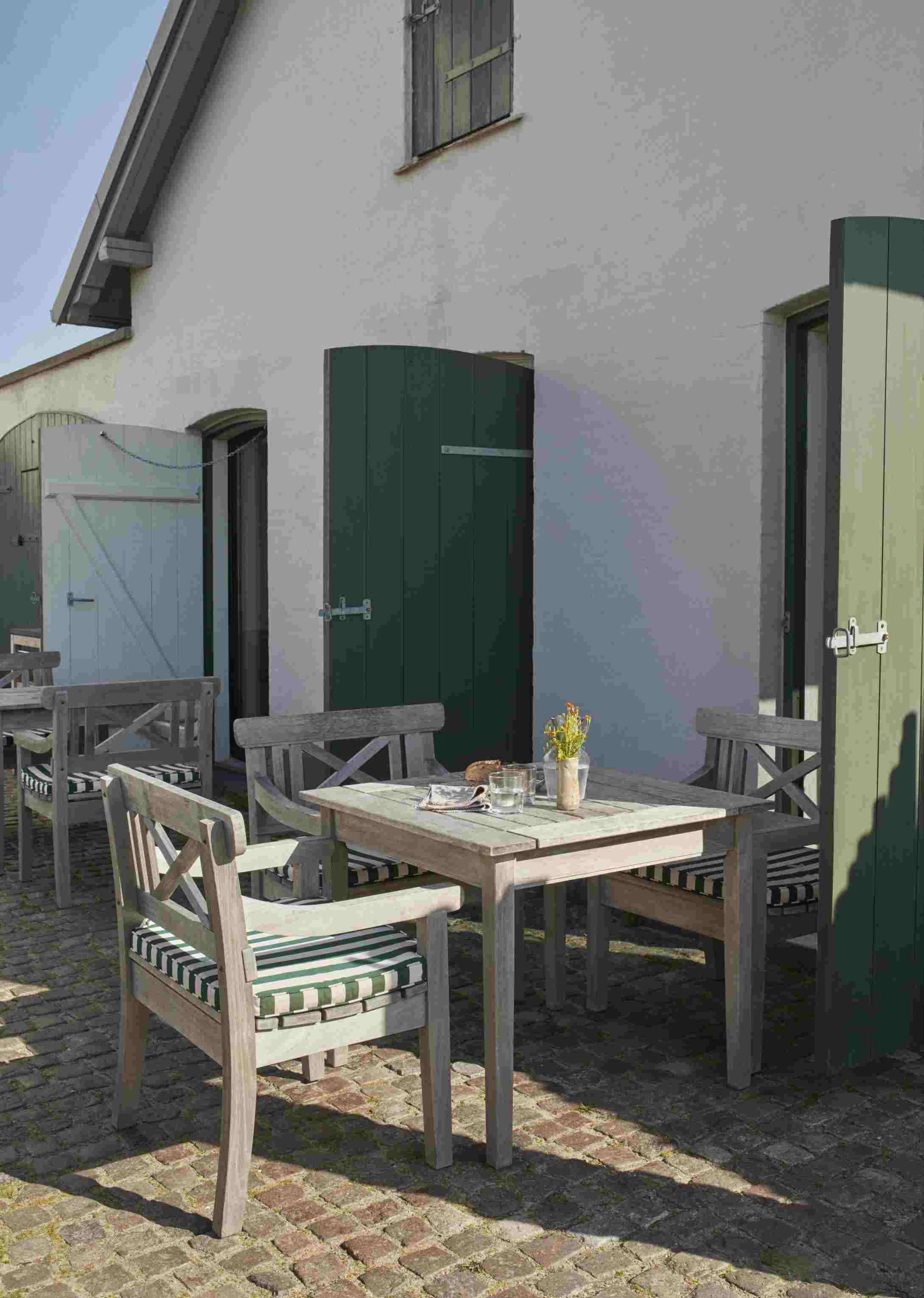 Drachmann Stuhl mit Sitzkissen in Helles Apricot und Dunkelgrünen Streifen auf einer Terrasse.