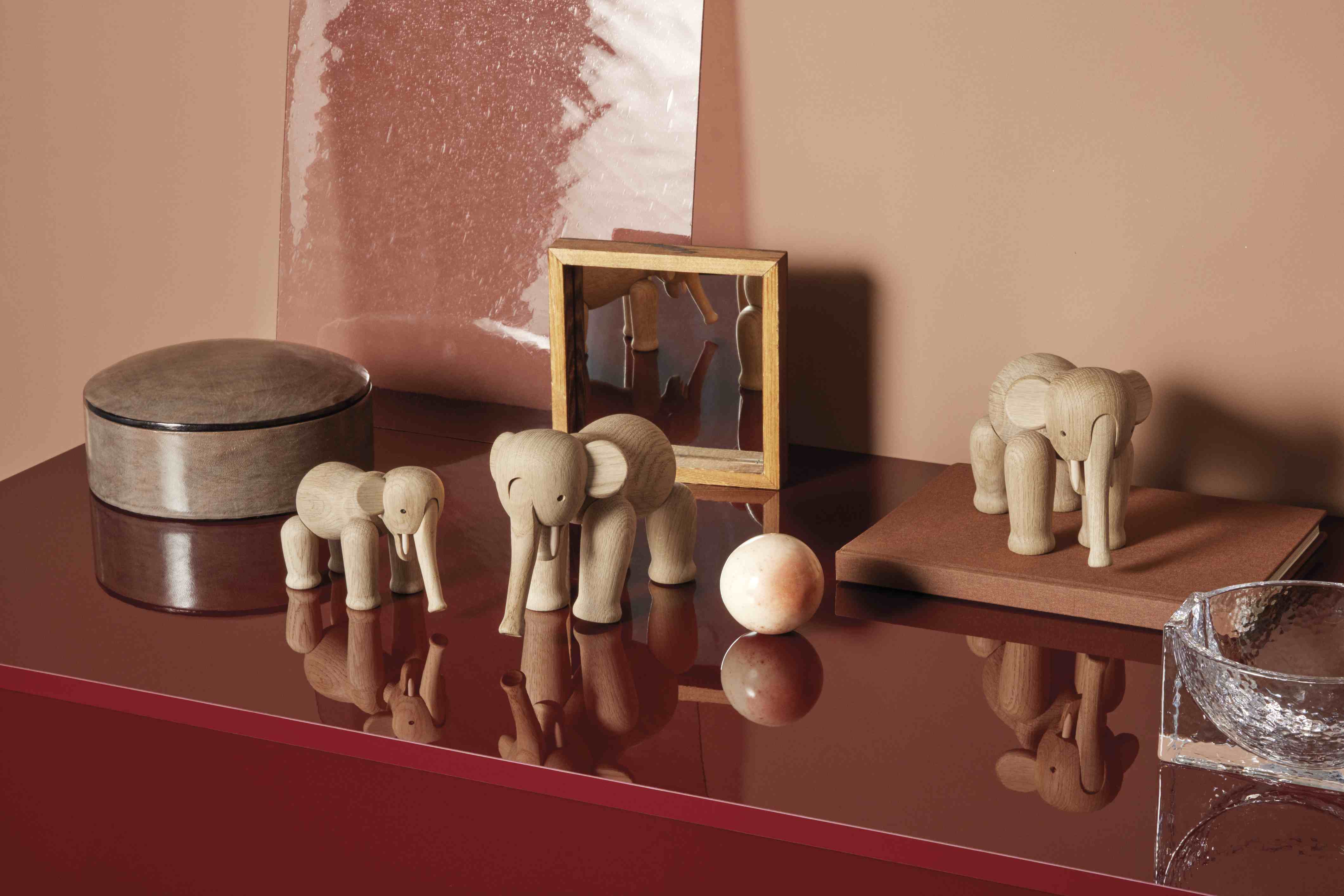 Hölzerne Elefantenfiguren in verschiedenen Größen als Dekoration auf einem roten Tisch, skandinavisches Design.