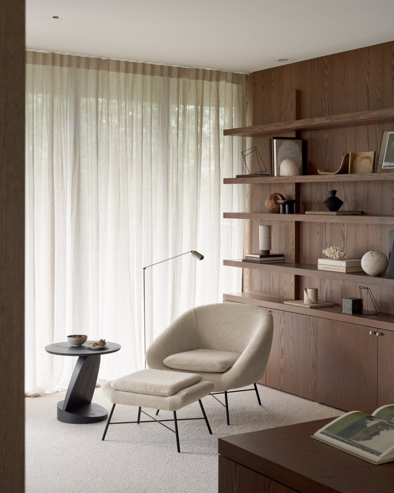 Beiger Barrow Fußhocker von Ethnicraft im Wohnzimmer mit Sessel und Bücherregal.