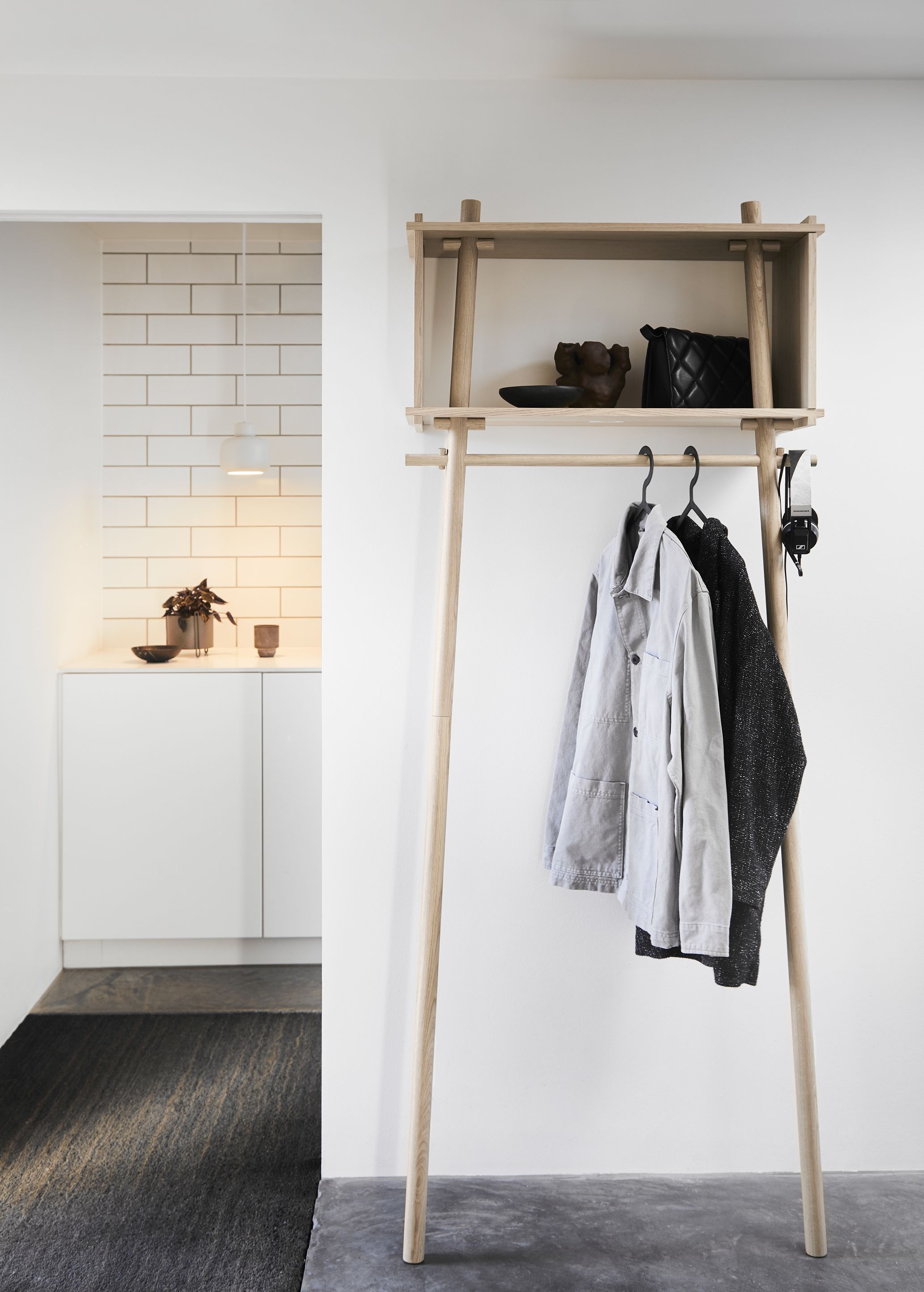 Hellele Holzgarderobe mit Ablage, Jacken, Handtasche und Kopfhörer; im Hintergrund Stone Pendant Pendelleuchte klein von Woud sichtbar.