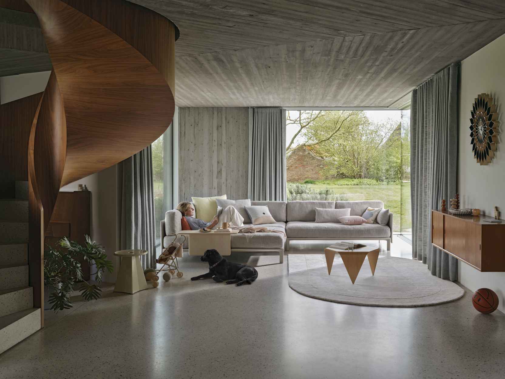 Helle Wohnraum-Szene mit Vitra Anagram Sofa, Frau, Hund und Wendeltreppe für ein modernes Wohnambiente.
