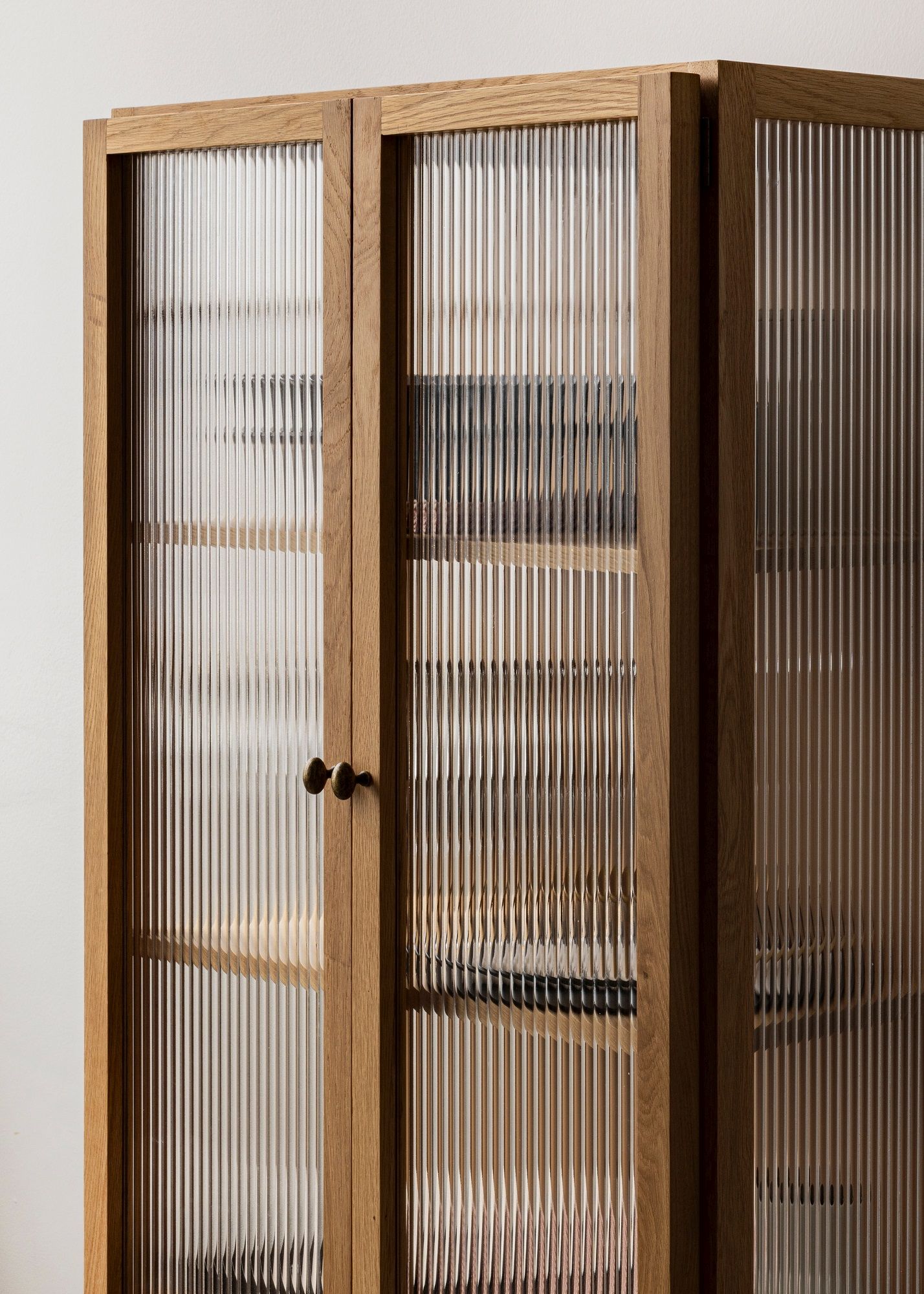Nahaufnahme des Curiosity Cabinet Schranks von Audo Copenhagen mit geriffeltem Glas und Holzrahmen.