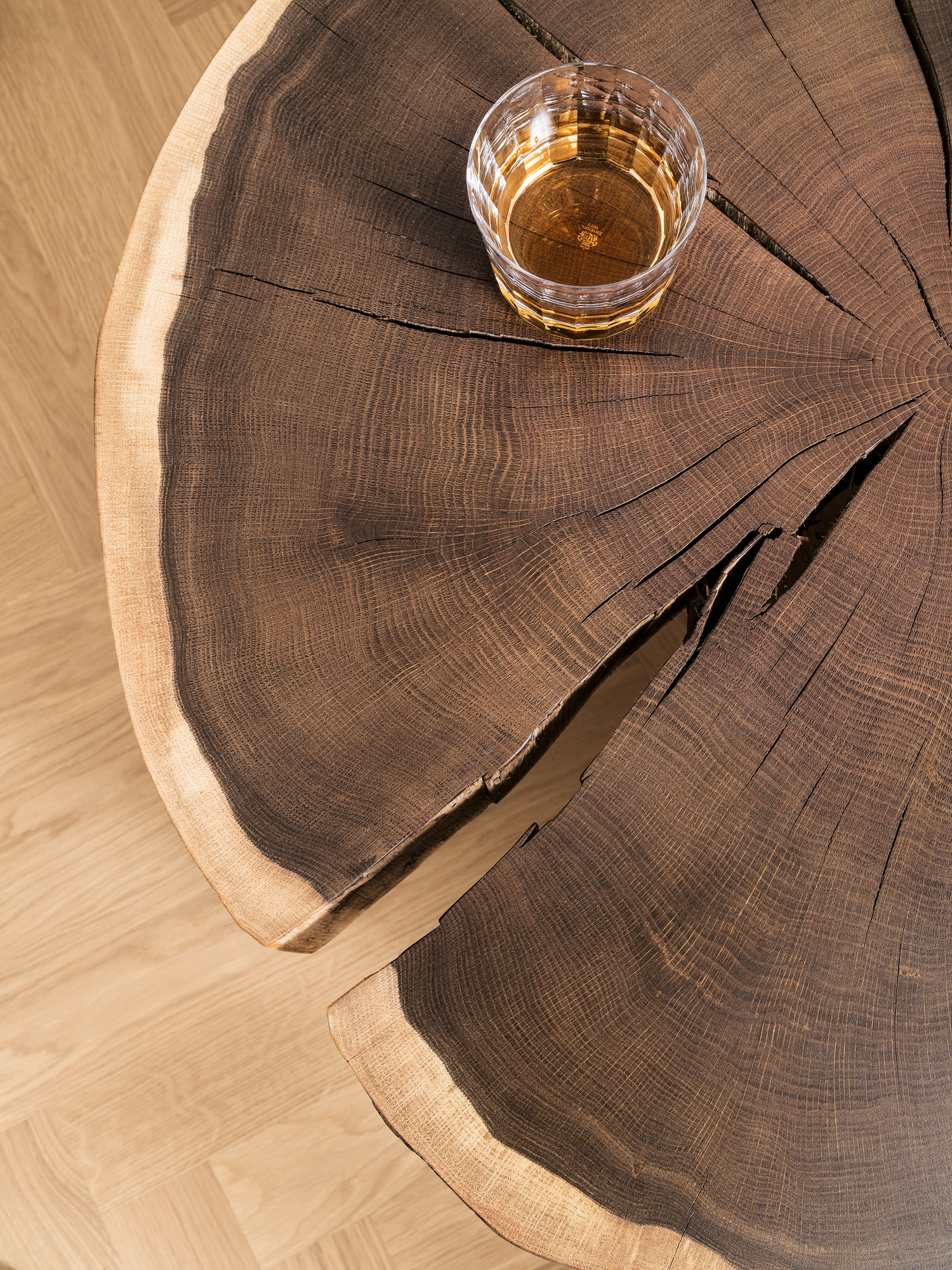 Detailaufnahme Janua Stomp Beistelltisch H52 roh: Massiver Holztisch mit Baumscheiben-Optik und einem Glas Whiskey.