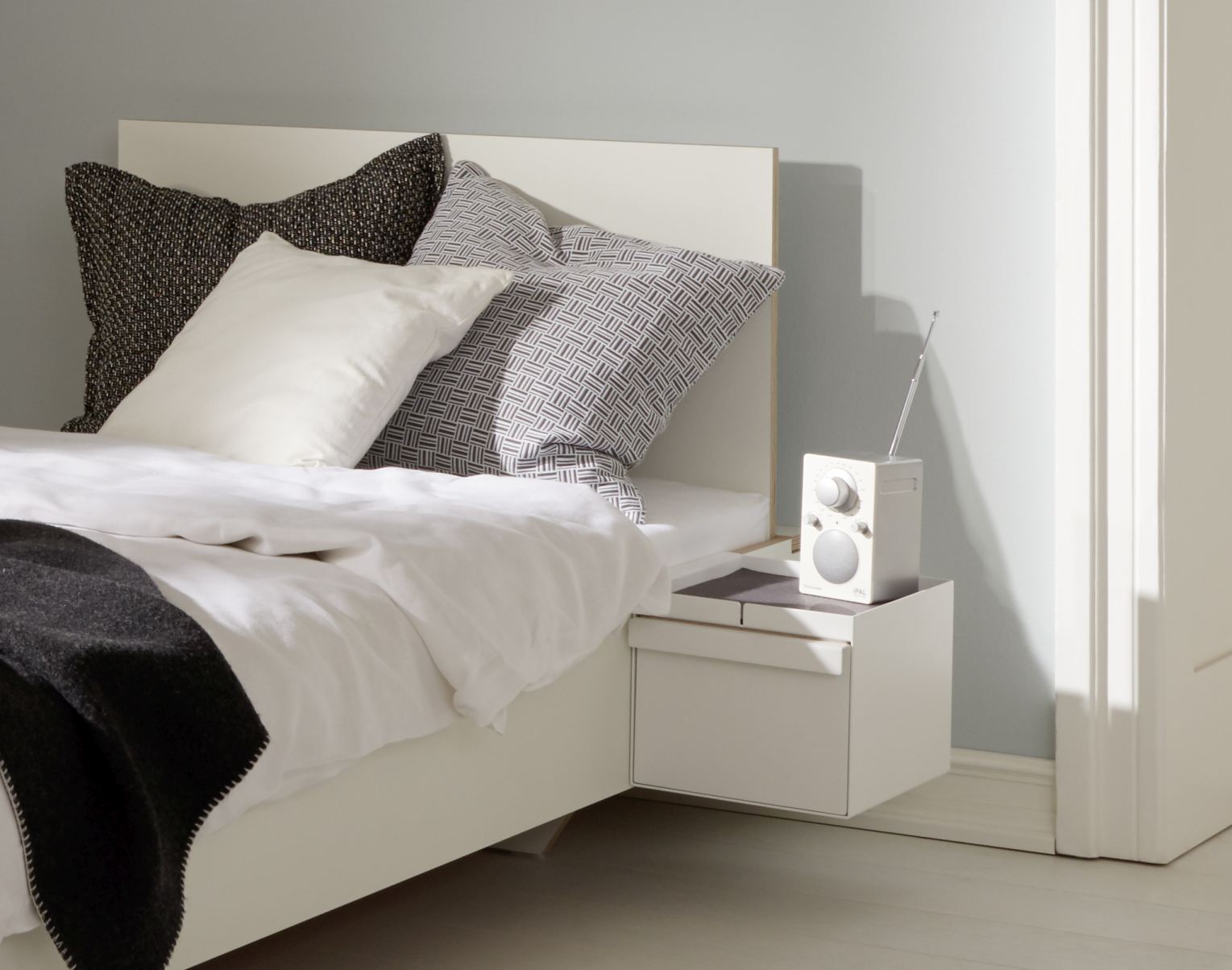 Weißes Flai Add-On Element von Müller Möbelwerkstätten mit Schubkasten als Nachttisch am Bett.