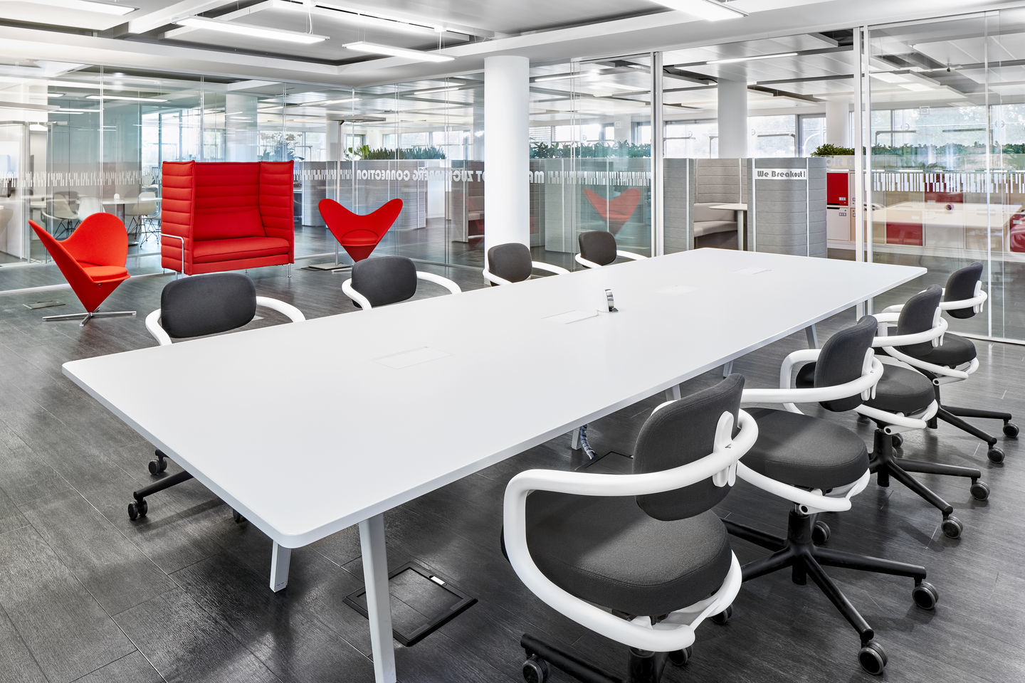 Büroraum mit weißem Konferenztisch und Bürostühlen, im Hintergrund rote Heart Cone Chairs von Vitra.