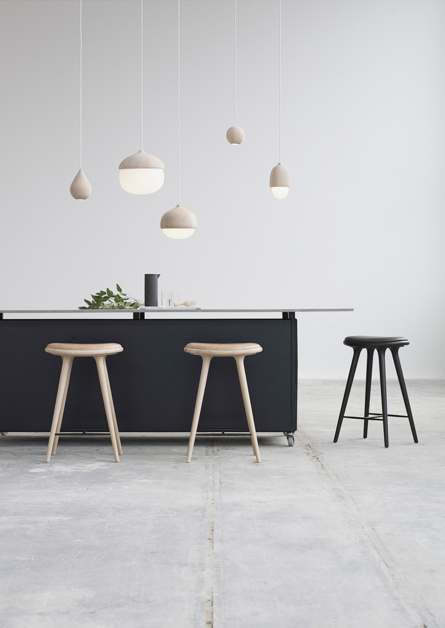 Innenaufnahme mit Liuku Base Ball Linde Pendelleuchten und Holzstühlen an einer Küchentheke.