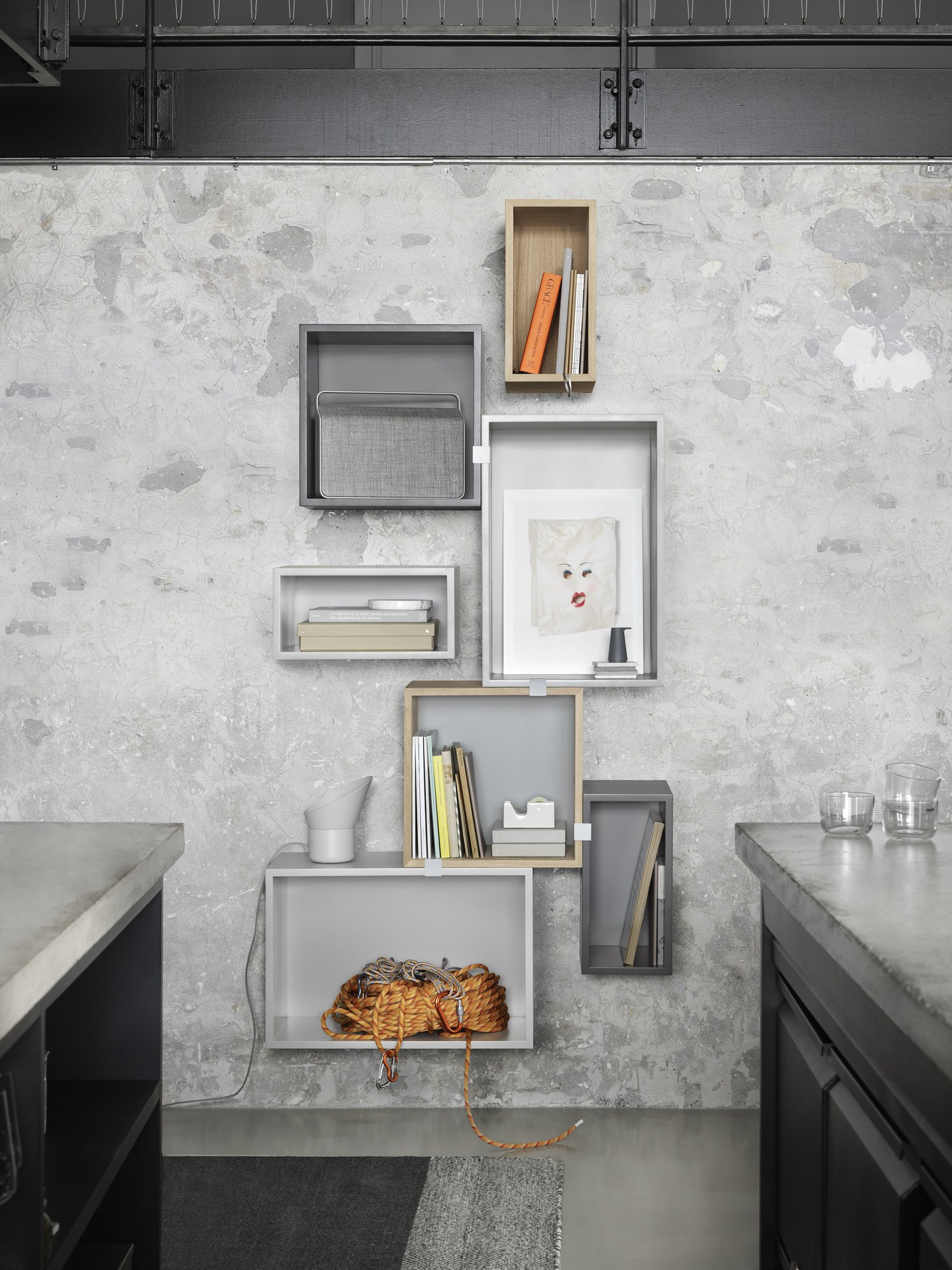Muuto Stacked Regalsystem 2.0 an einer Betonwand mit Deko-Elementen, Bücher und Kletterseil in verschiedenen Farben.