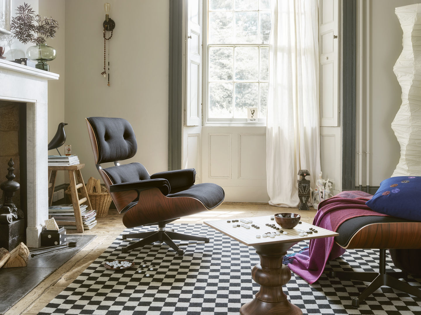 Wohnzimmer-Szene mit Vitra Eames Lounge Chair, Ottoman, Schachbrett-Teppich und einer Wooden Doll Katze als Dekoration.