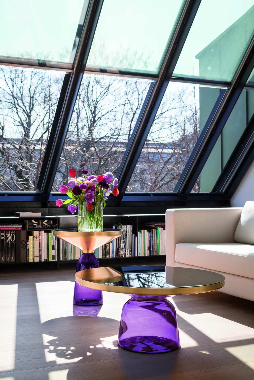 Lila Couchtische aus Glas und Metall mit Blumenstrauß vor Fenster in modernem Wohnzimmer.