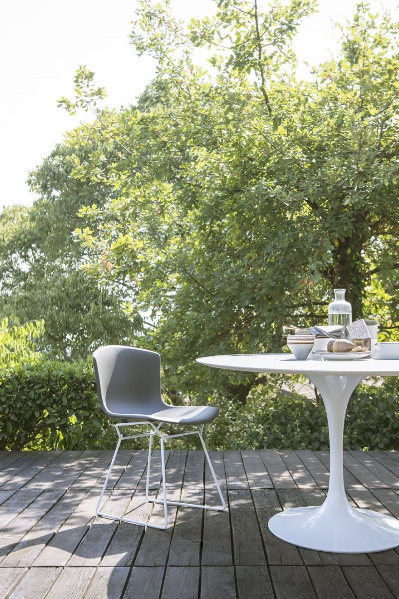 Grauer Design Stuhl und runder Esstisch für den Garten auf Holzterrasse im Grünen.