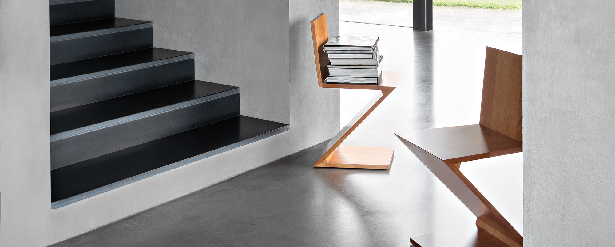 Cassina Zig Zag Stuhl aus Holz, modernes Designmöbel neben einer Treppe mit Büchern.