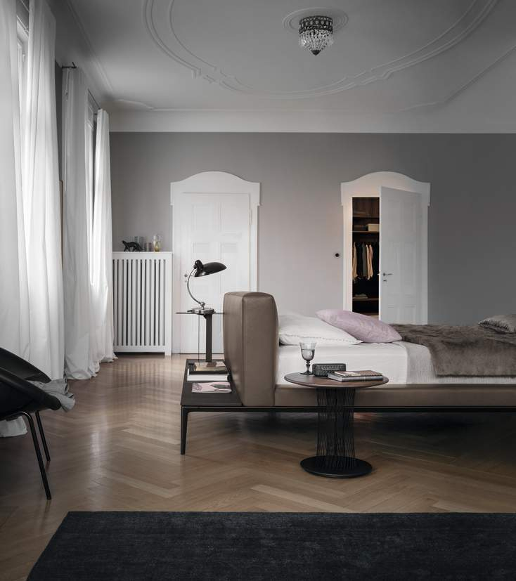Schlafzimmer Interieur mit Walter Knoll Bett, Nachttisch, Lampe und Teppich auf Parkettboden.
