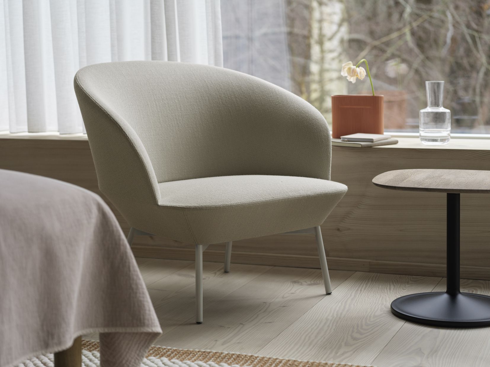 Beiger Oslo Lounge Chair Sessel von Muuto mit hellen Metallbeinen neben kleinem Holztisch und Fenster.