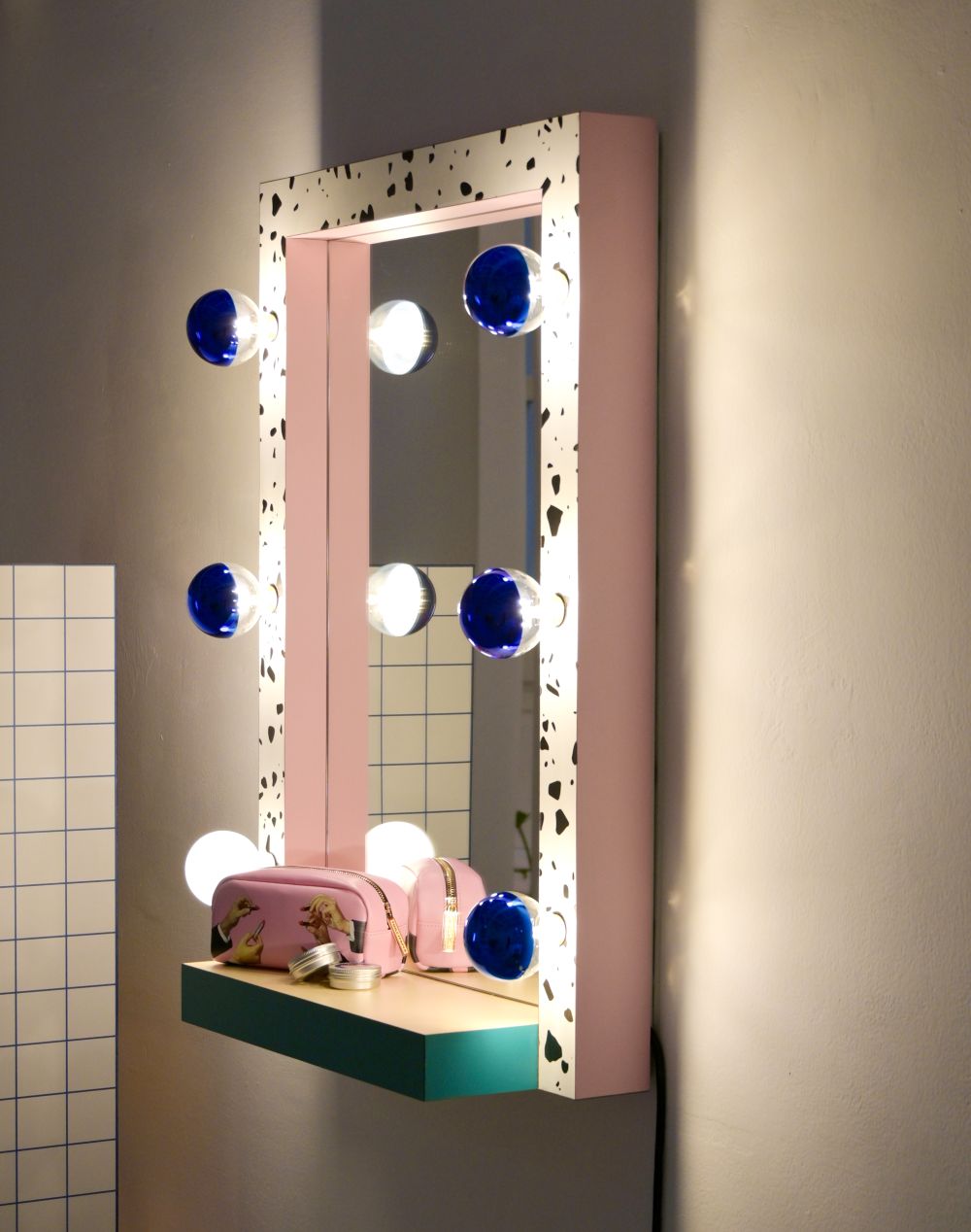 Supermirror Spiegel von Seletti mit rosa Rahmen, Terrazzo-Muster, blauen und weißen Glühbirnen und Ablage.