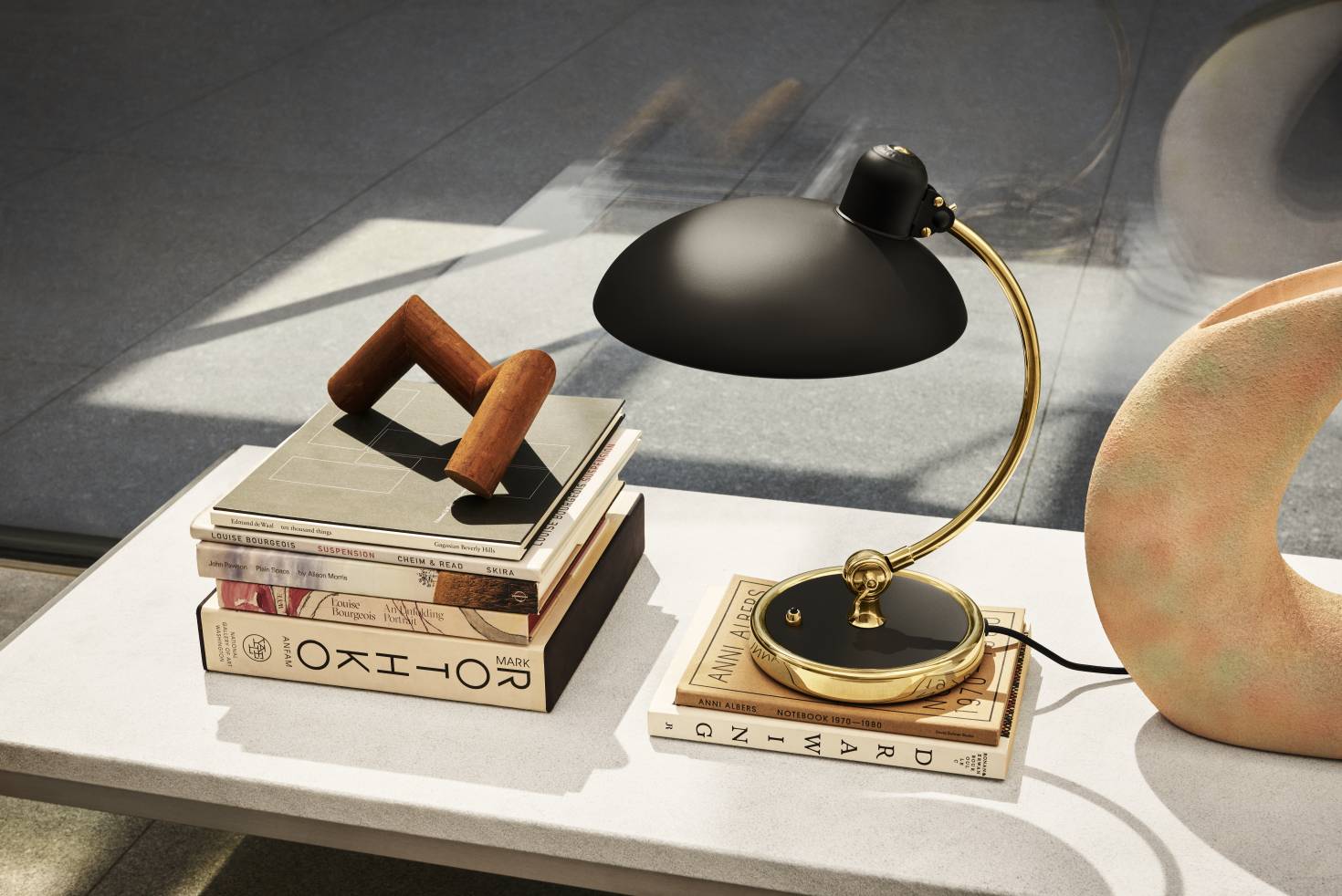 Nahaufnahme einer schwarzen Schreibtischlampe mit goldenem Gestell auf einem Tisch, Bücher und Deko-Elemente.