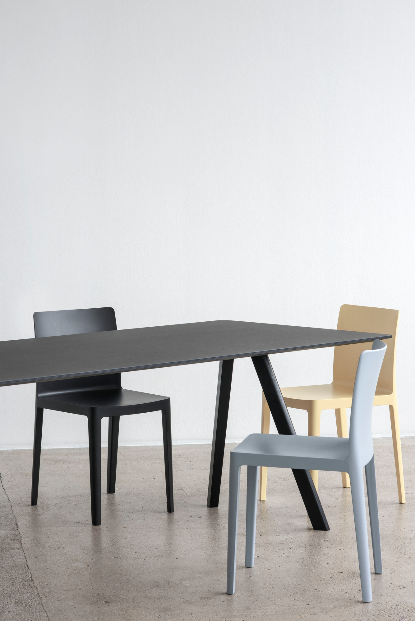 Schwarzer Copenhague Table CPH 30 Esstisch von Hay mit farbigen Stühlen vor einer weißen Wand.