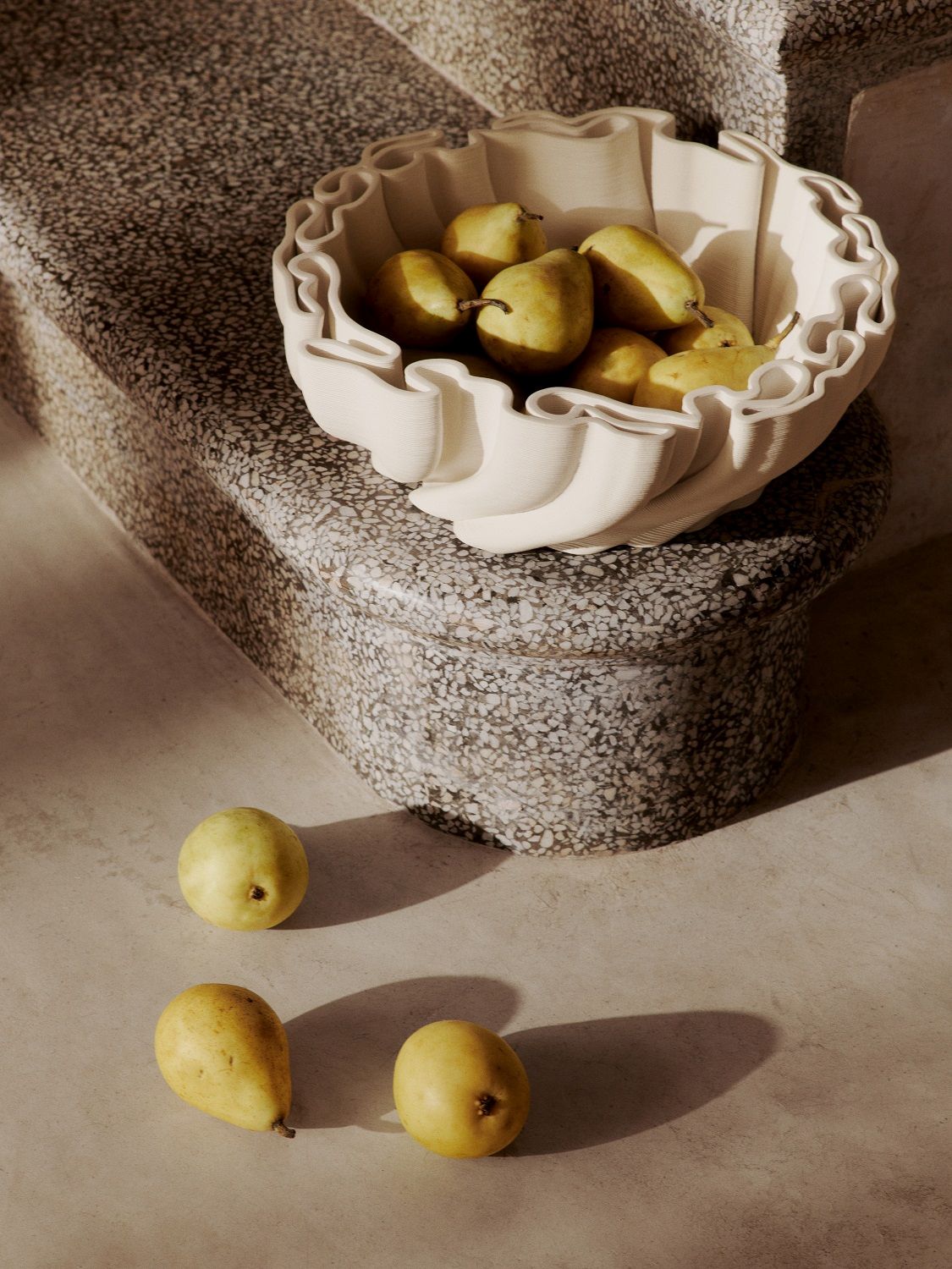 Off-white Dedali Bowl Schale von Ferm Living gefüllt mit gelben Birnen auf einer Steintreppe, moderne Tischdeko.